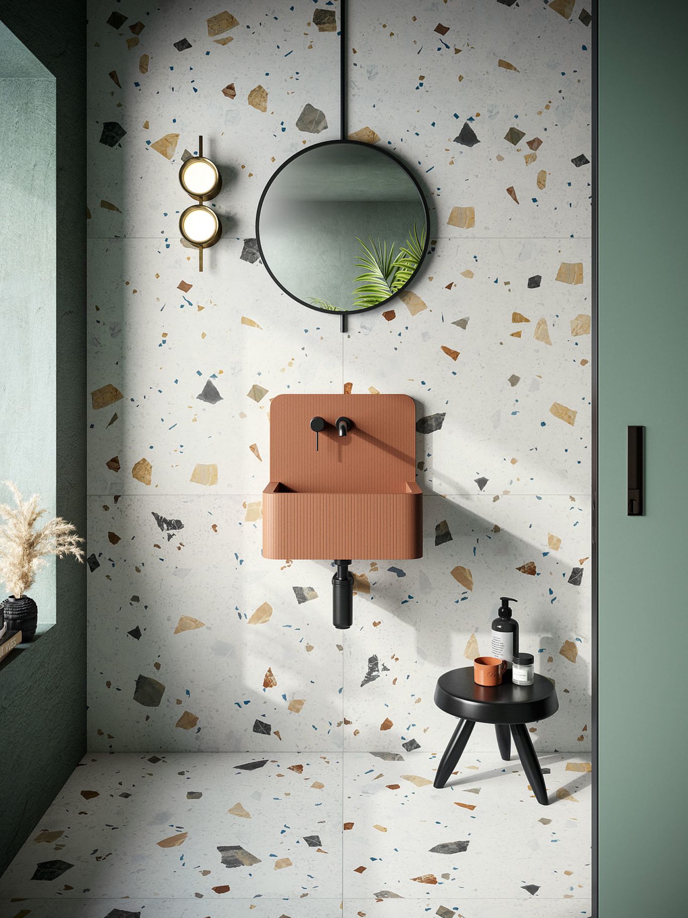 Tile en terrazzo sur le sol et le mur d'une petite salle de bain, avec un petit évier orange monté sur le mur et un miroir noir rond.