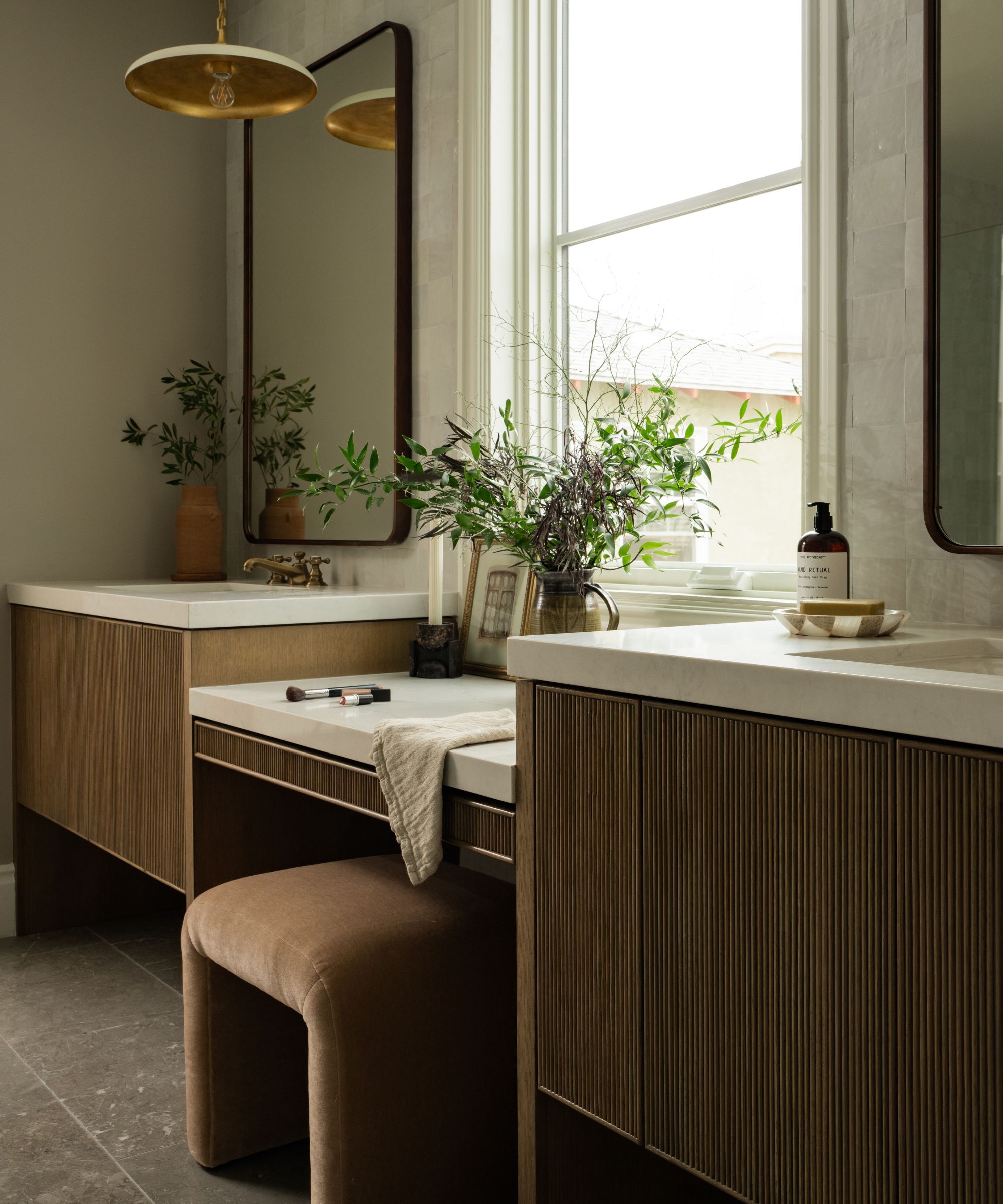 Salle de bain organique avec comptoir en marbre et armoires cannelées marron, plantes et suspension