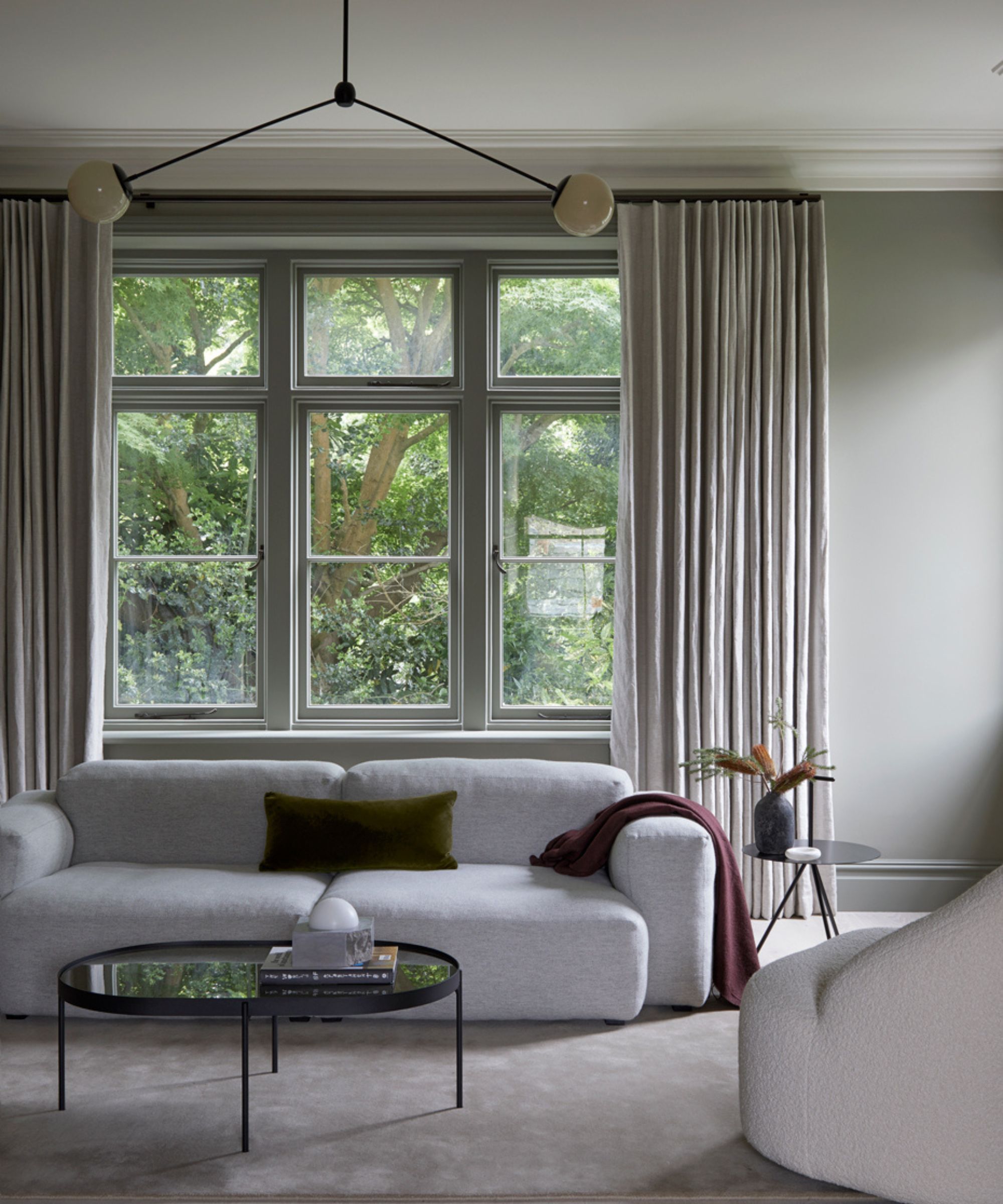 salon neutre avec murs gris, mobilier minimaliste moderne et grande fenêtre avec rideaux neutres