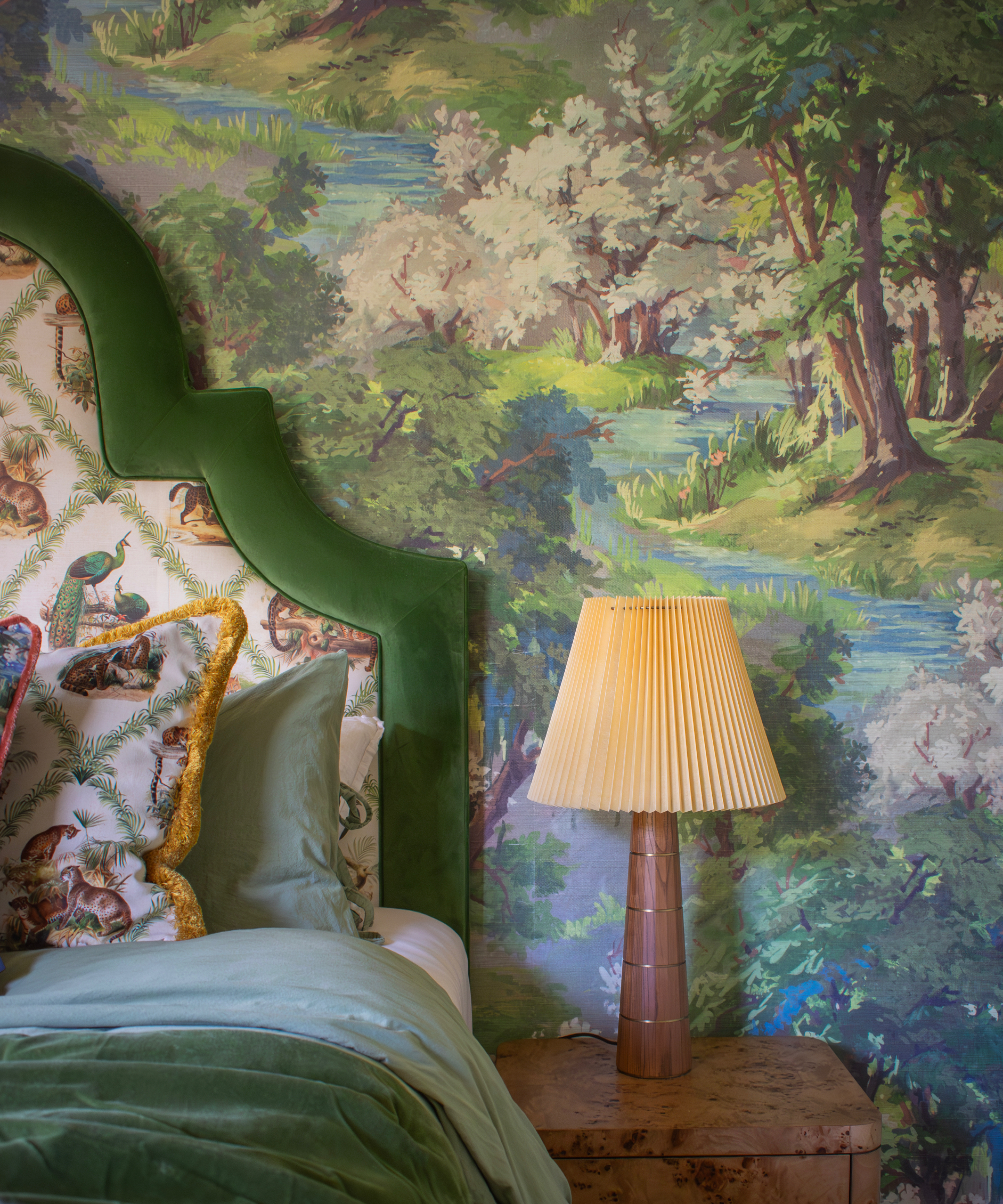 chambre à coucher avec bois vert / forêt papier peint peint mural avec une tête de lit incurvée avec garniture verte en velours, table de chevet et lampe, literie verte