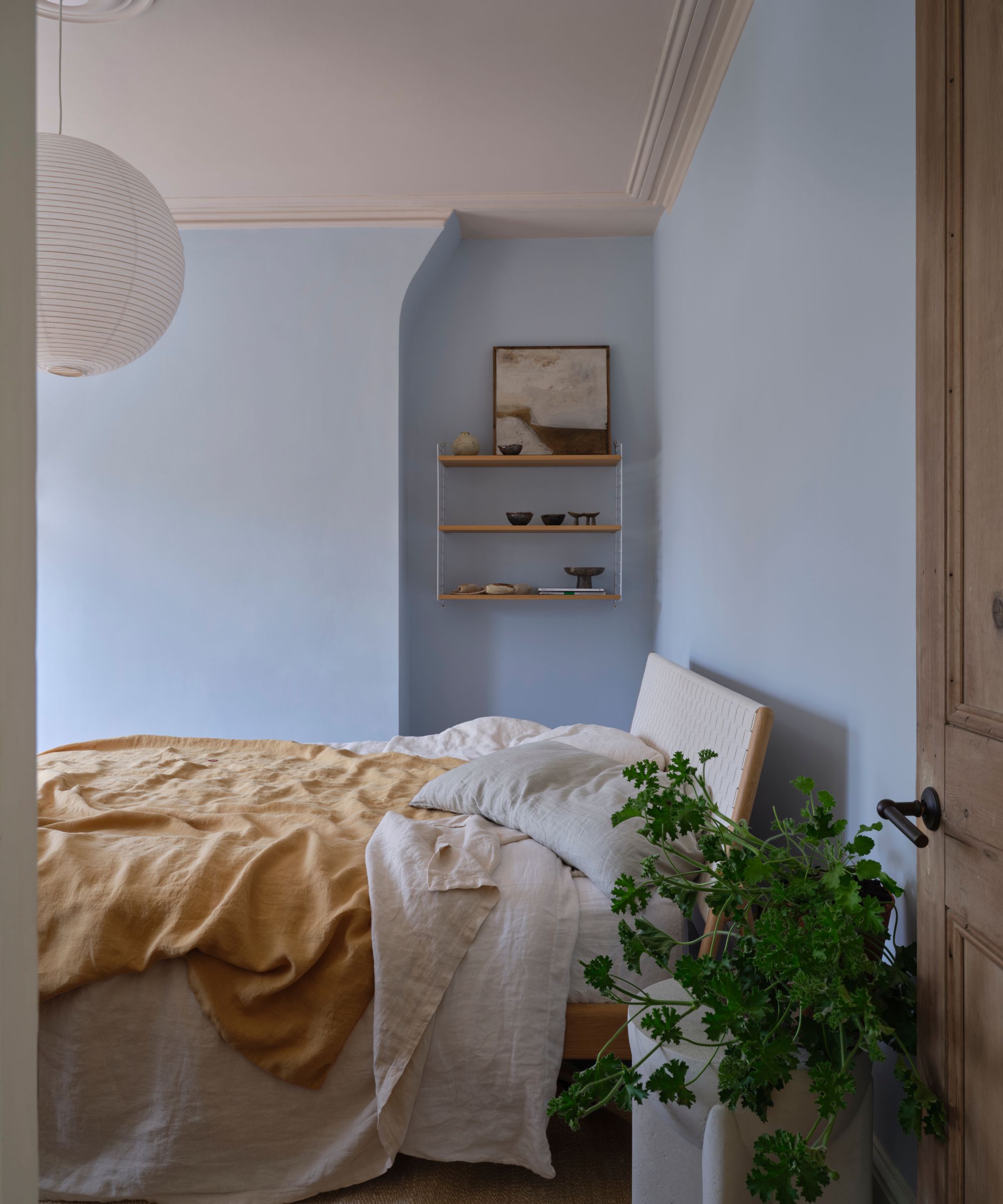 chambre à coucher avec murs bleu clair, literie neutre et planche à intermédiaire dans le coin