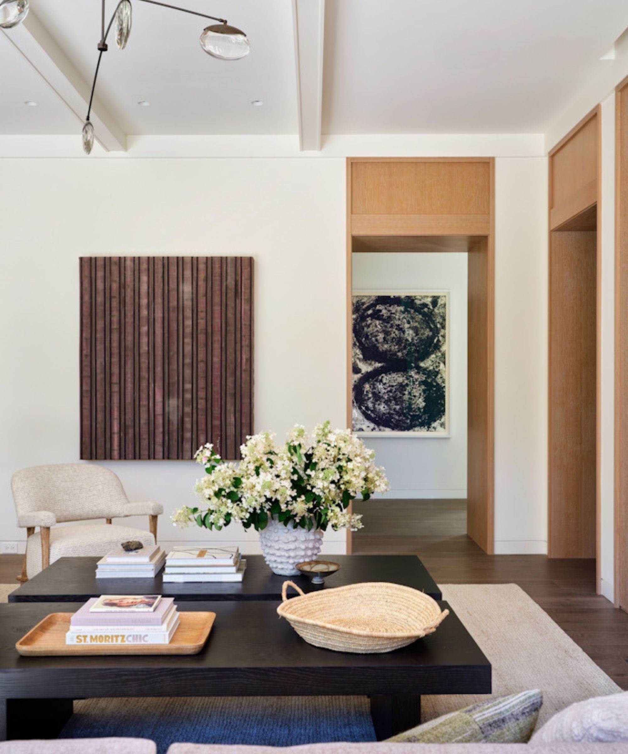 salon blanc avec décor moderne, table basse noire, œuvres d'art abstraites, tapis neutre avec fauteuil neutre