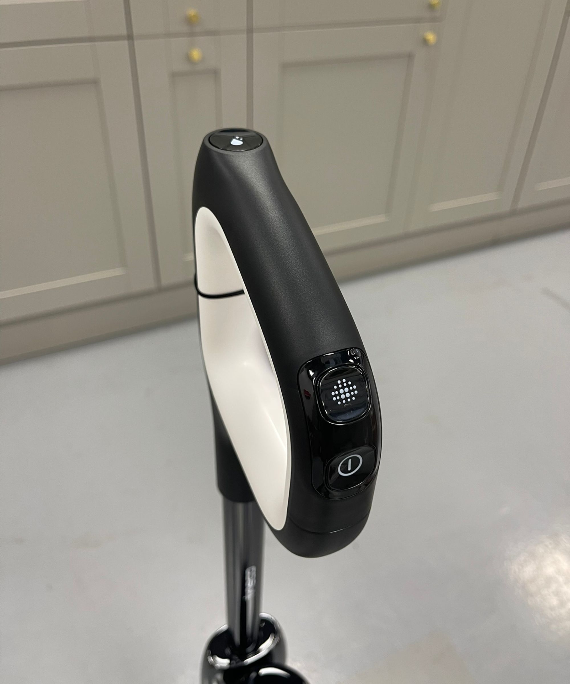 Closeup of the Black and White Tineco Floor One Stretch S6 Handle montrant trois boutons: ON / OFF, commutateur de mode et autonettoyant contre le sol gris et les armoires au centre de test du futur
