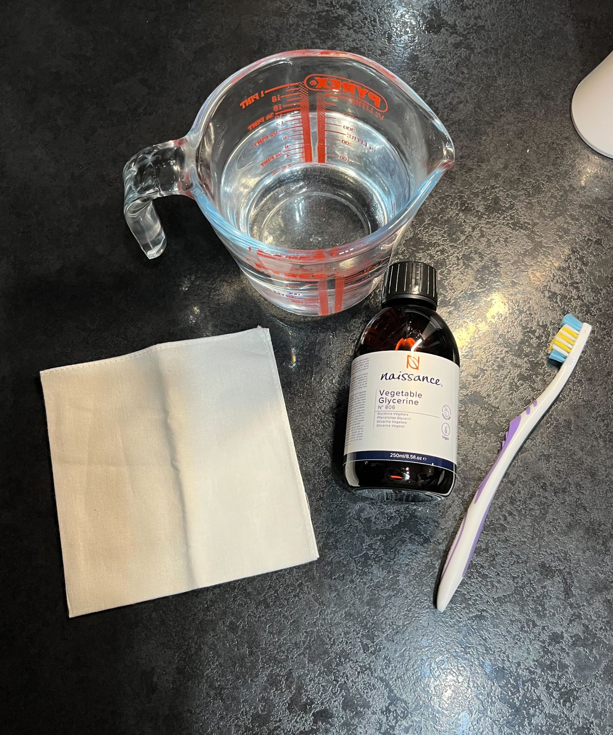 Une cruche en verre remplie d'eau, une bouteille de glycérine, une vieille brosse à dents et un tissu blanc