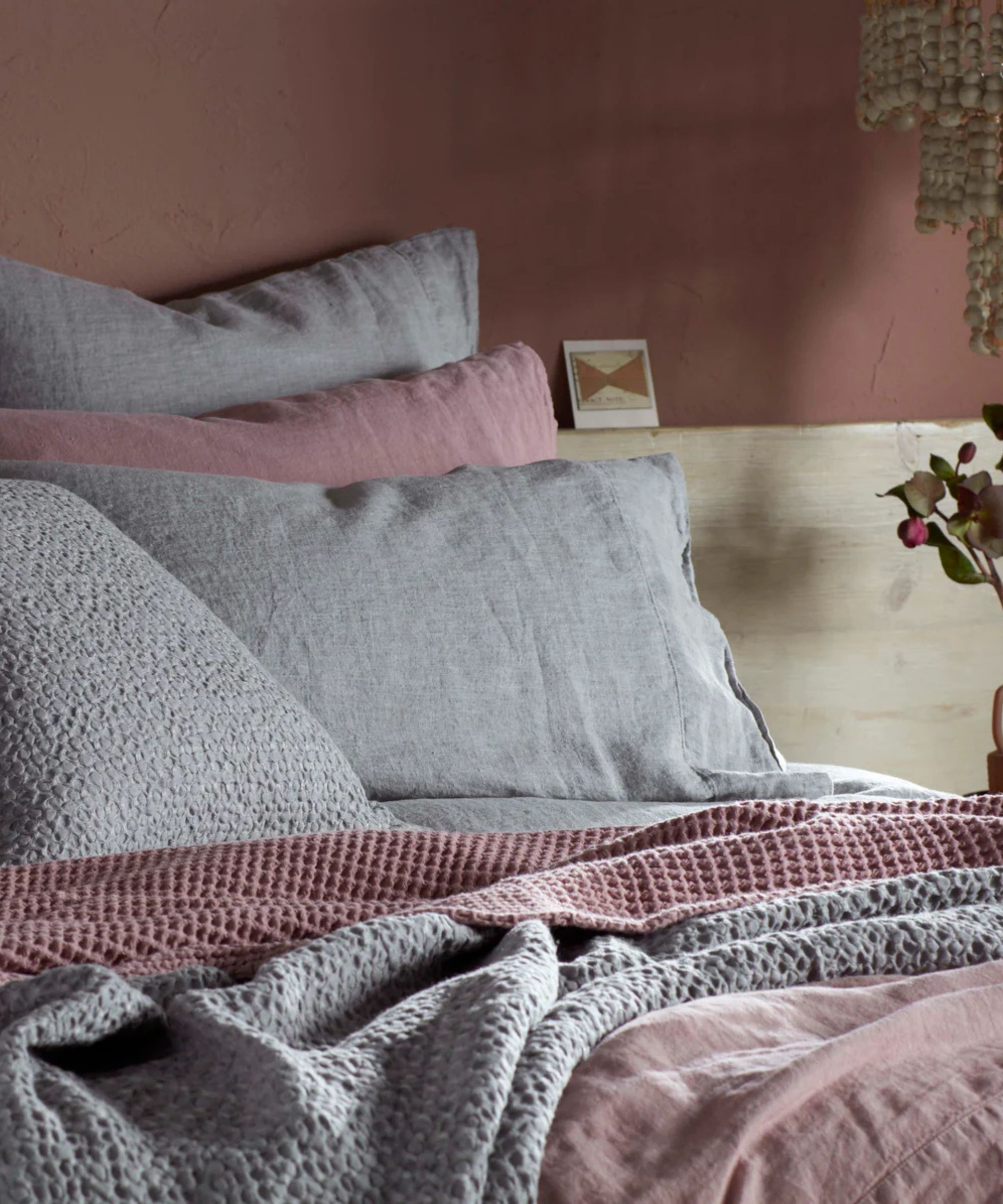 Des draps et des couvertures roses et gris sur un lit contre un mur rose.