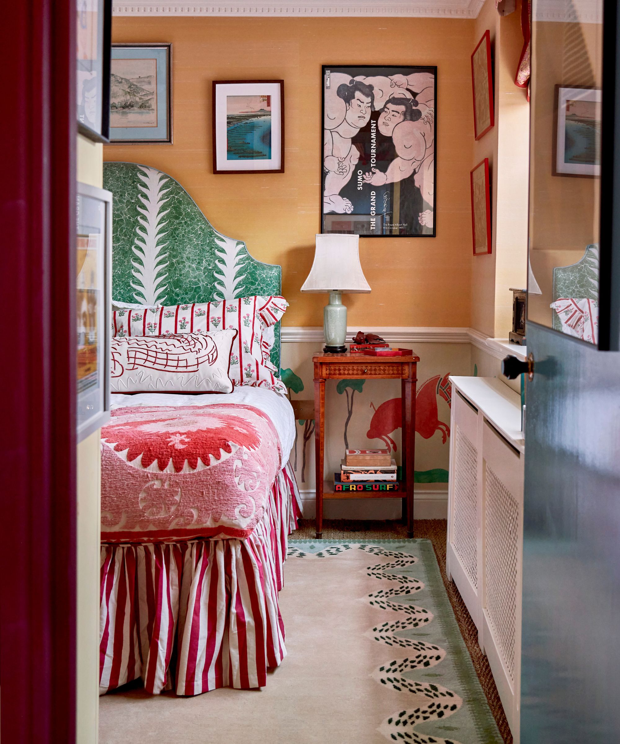 Peine de chambre à coucher éclectique dans une orange douce avec une jupe de lit à rayures, une tête de lit à motifs verts et un grand tapis
