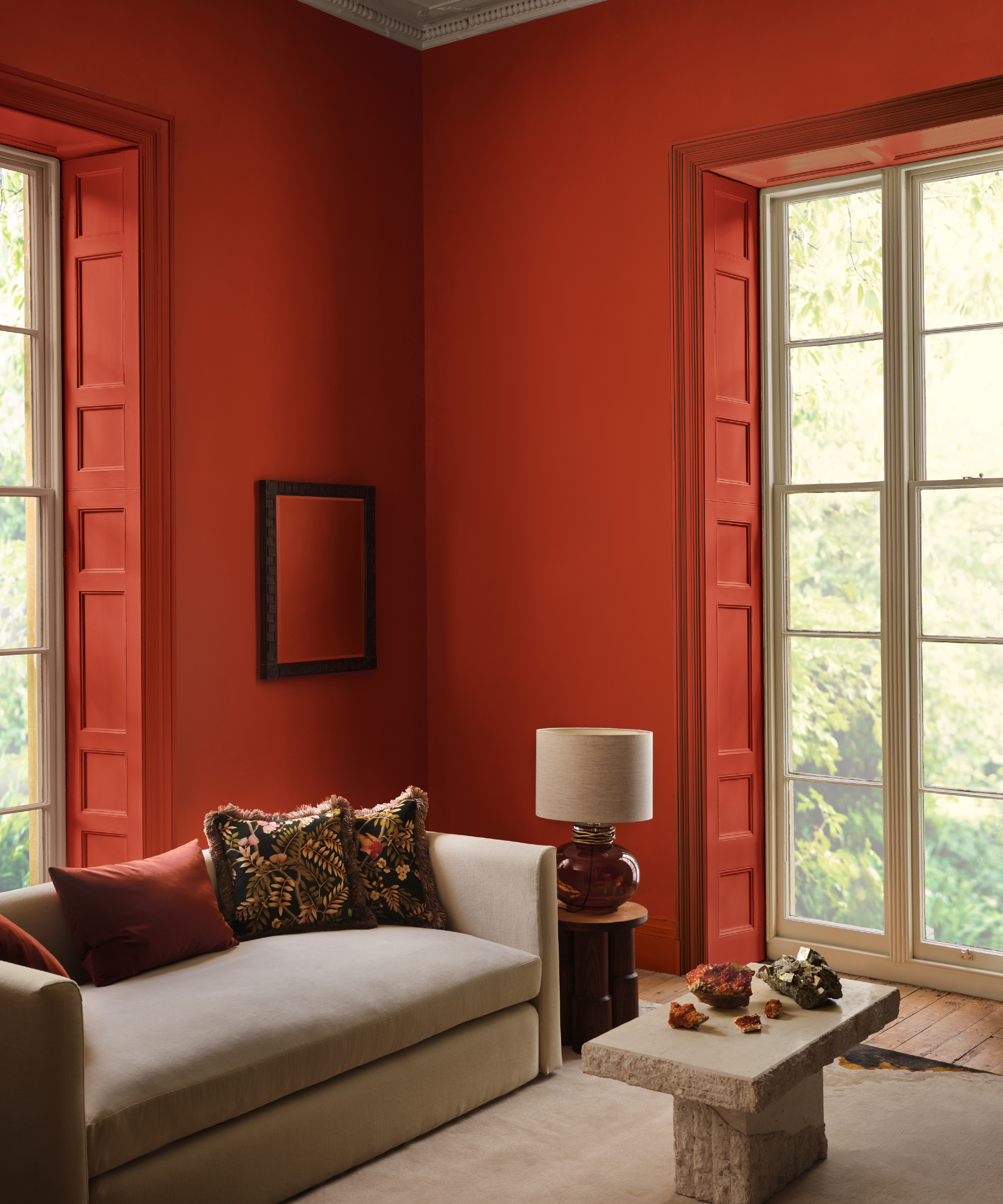Salon moderne avec murs et volets rouges en brique, canapé taupe et tapis crème, table basse en pierre, œuvres d'art, lampe, oreillers à motifs de canapé