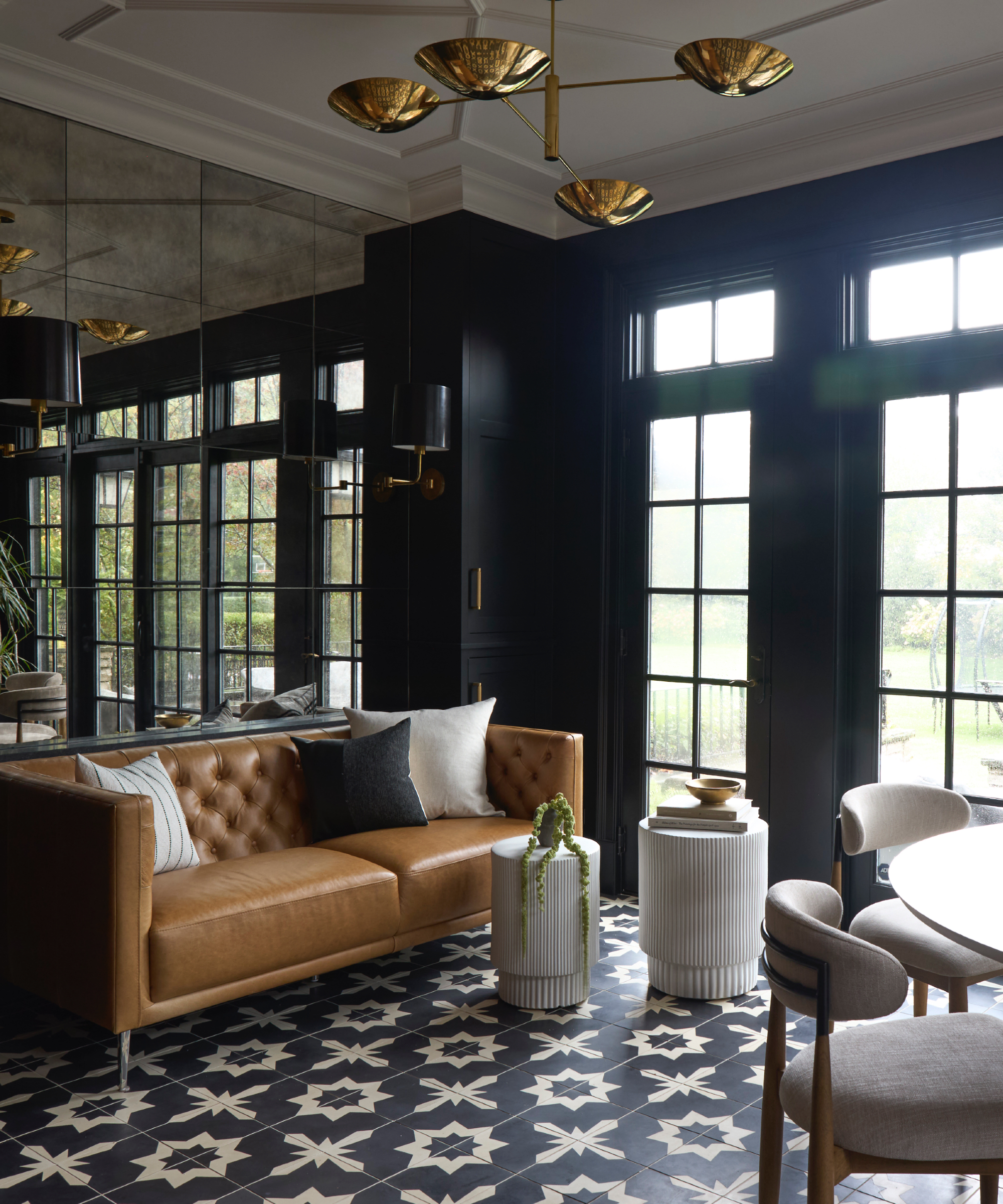 Espace vivant et salle à manger avec plancher carrelé noir et blanc, canapé en cuir beige, pendentif en laiton, murs noirs, miroir