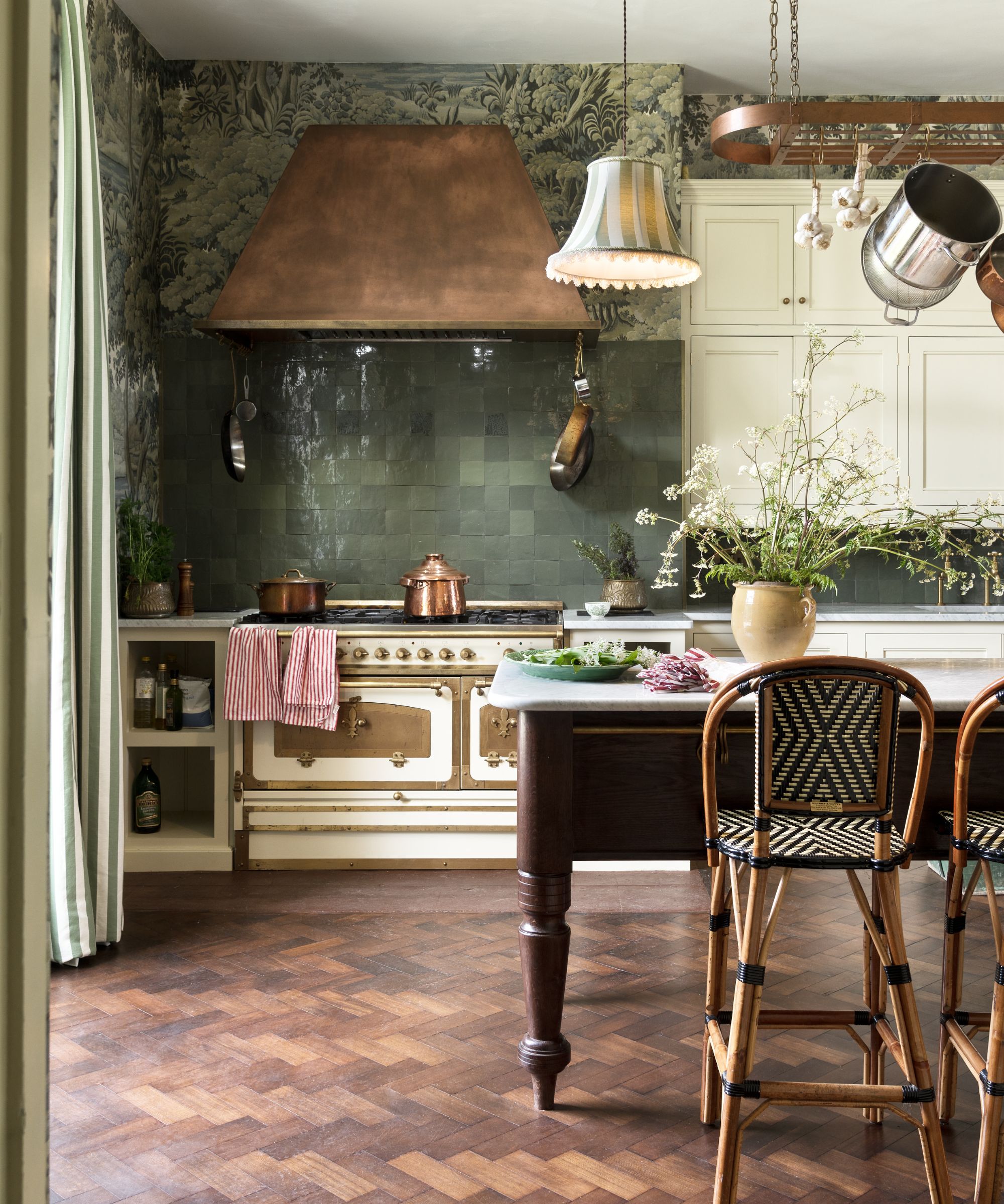 Dosseret carrelé vert avec plancher en parquet en bois, table de cuisine en bois, capuchon en cuivre, casseroles en cuivre et armoires à crème