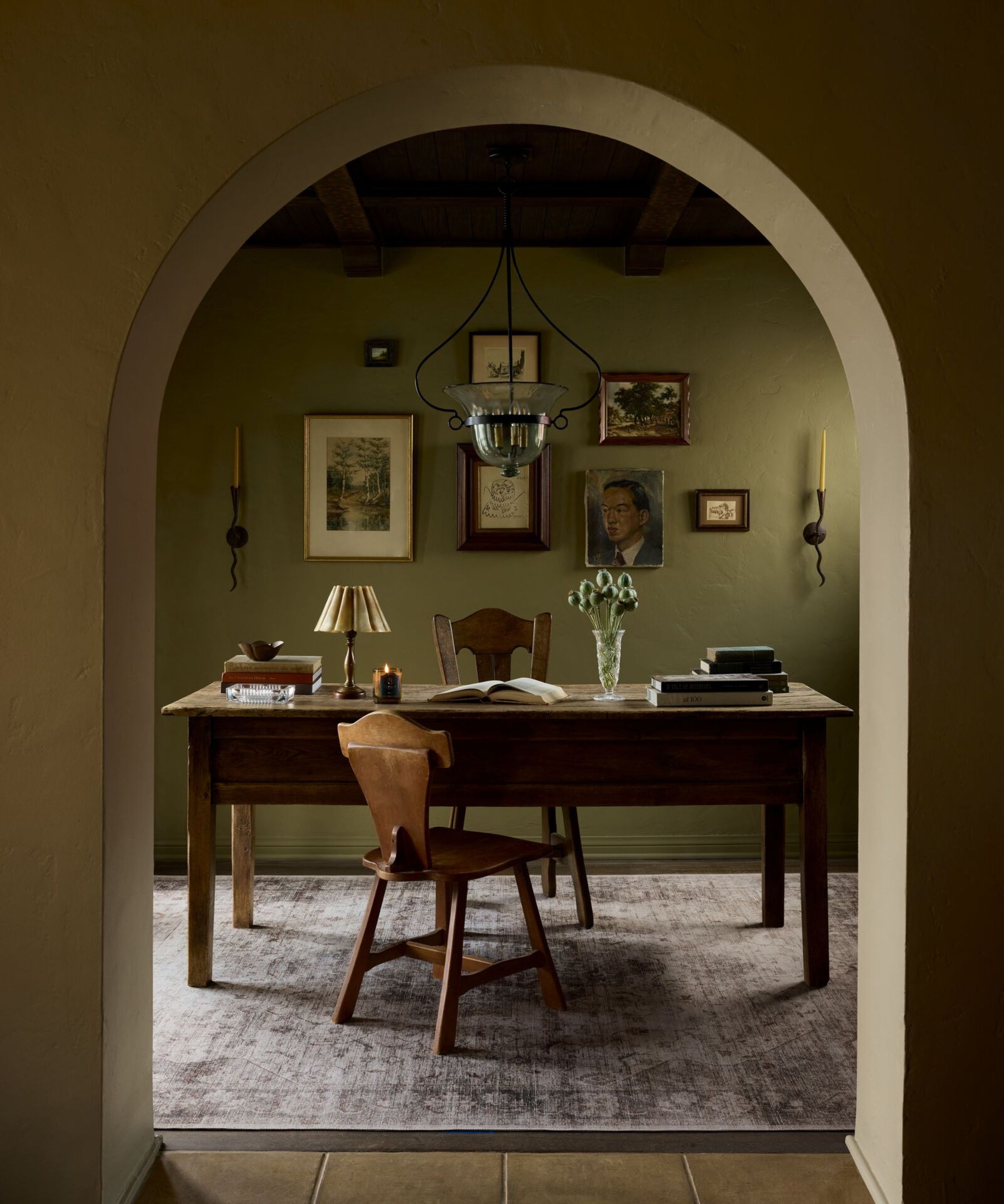 Porte arquée qui montre un bureau vert avec des peintures antiques sur le mur, un bureau en bois et des chaises et un tapis motivé