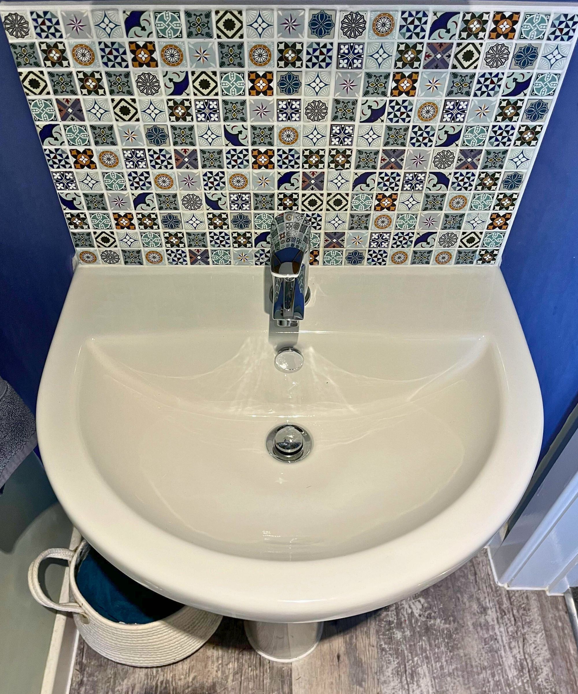 Évier de salle de bain blanc propre avec dosseret en mosaïque, Tapisseur chromé et peinture murale bleue