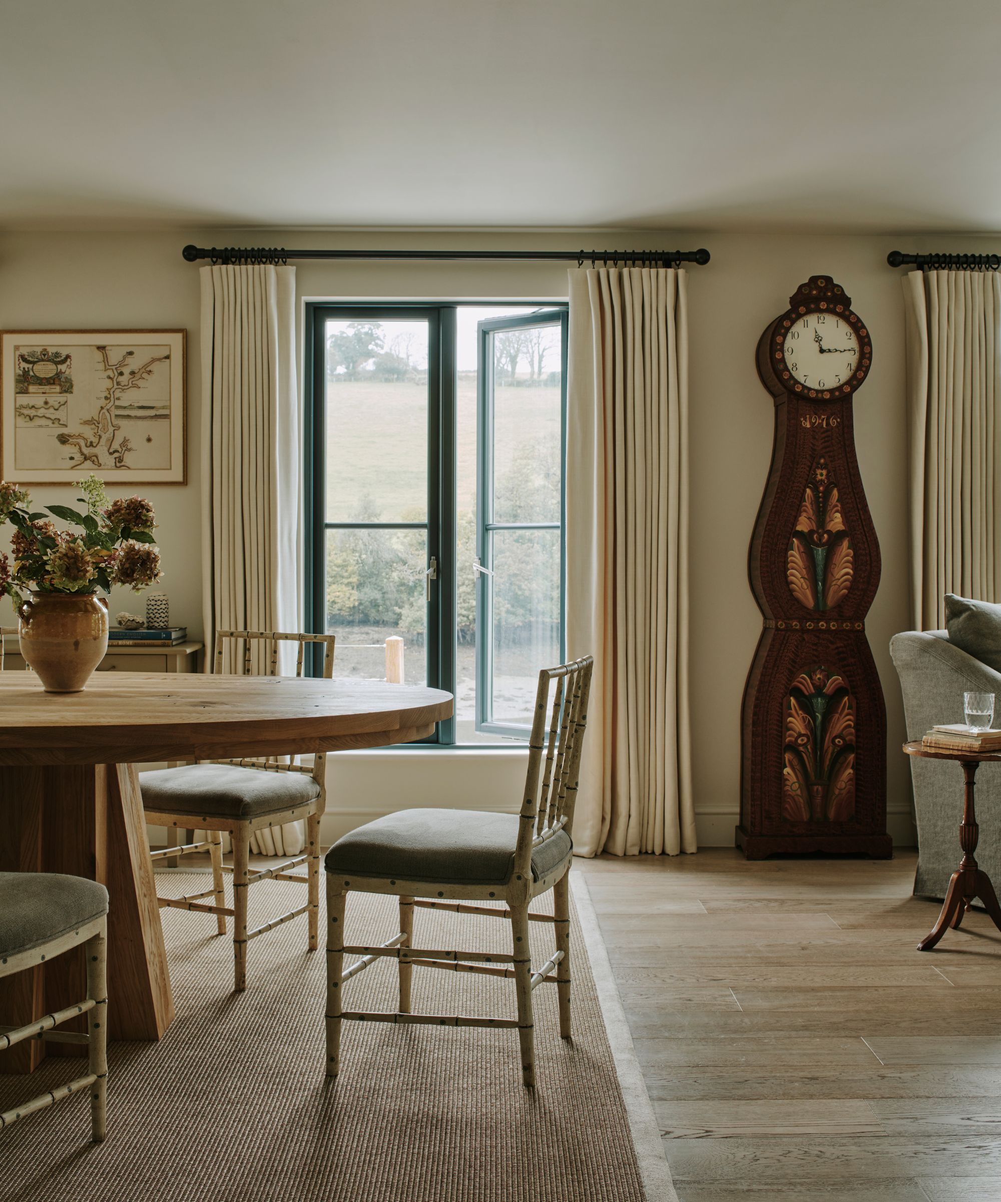 Salle à manger neutre avec une grande table ronde en bois et une grande horloge de grand-père en acajou orné