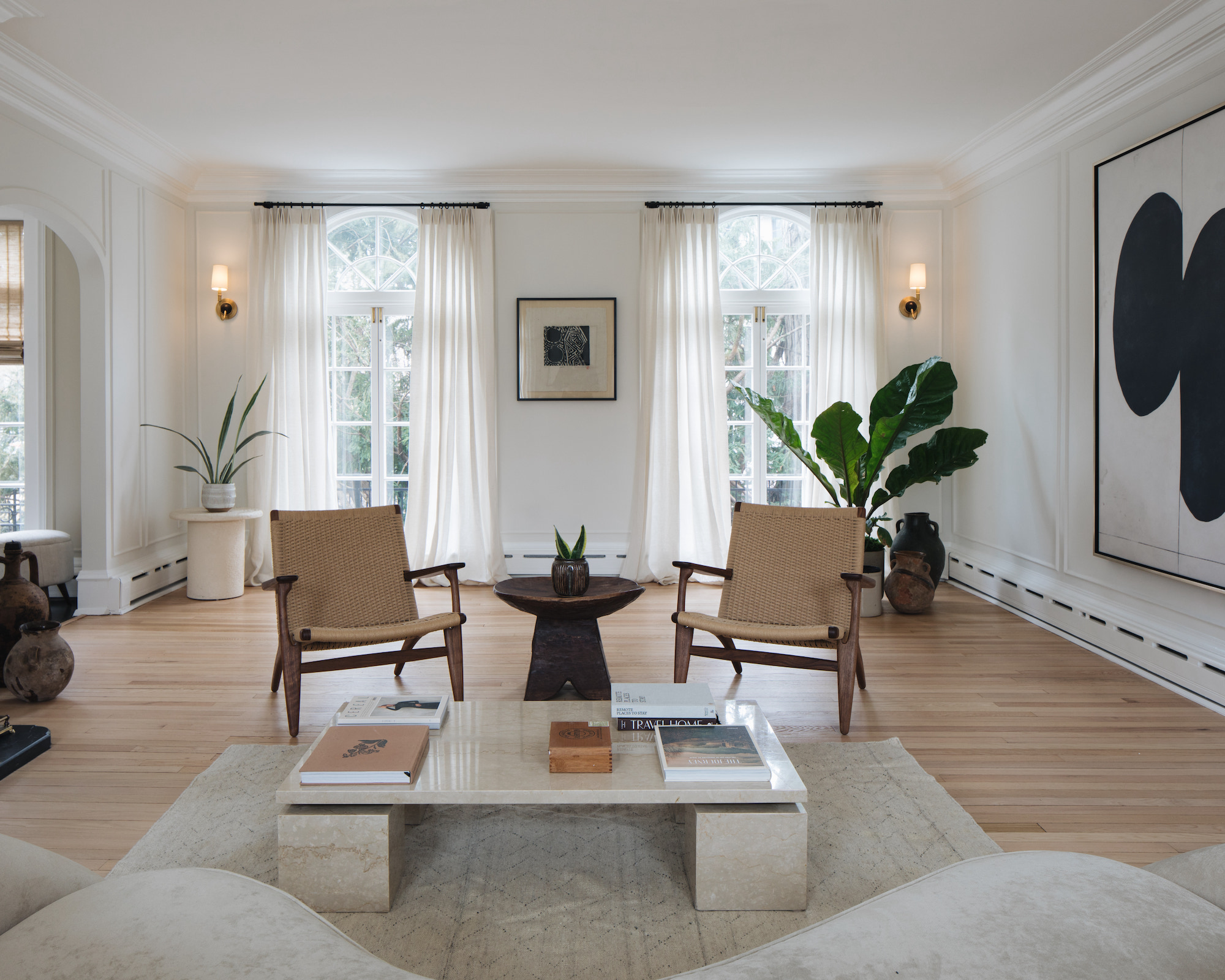 Salon neutre avec table basse, fauteuils, tapis de zone, grandes œuvres d'art et deux fenêtres vêtues de rideaux entièrement longueur
