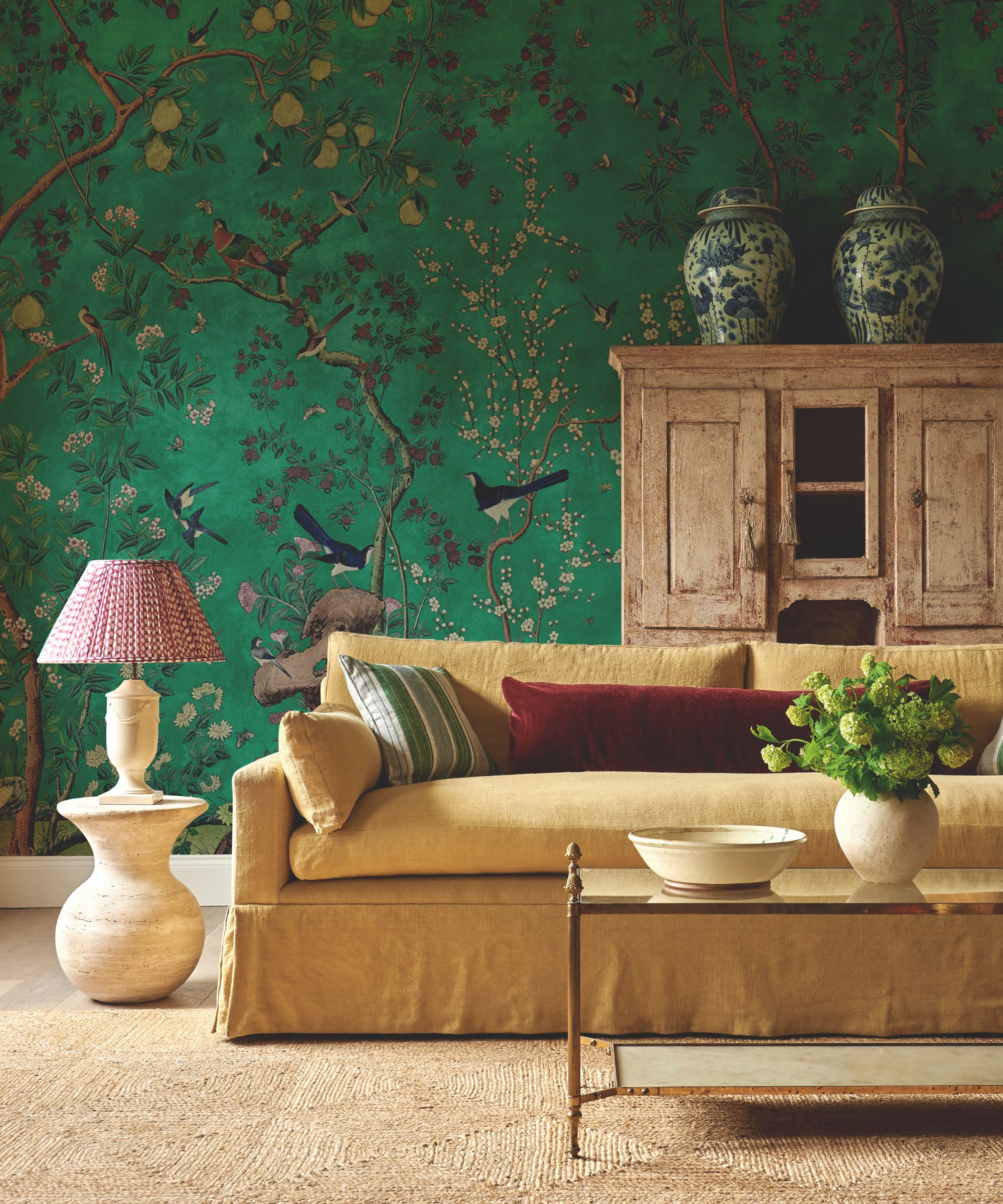 salon vert avec murale murale avec arbres et oiseaux et grand canapé en lin et armoire autoportante en bois ancien