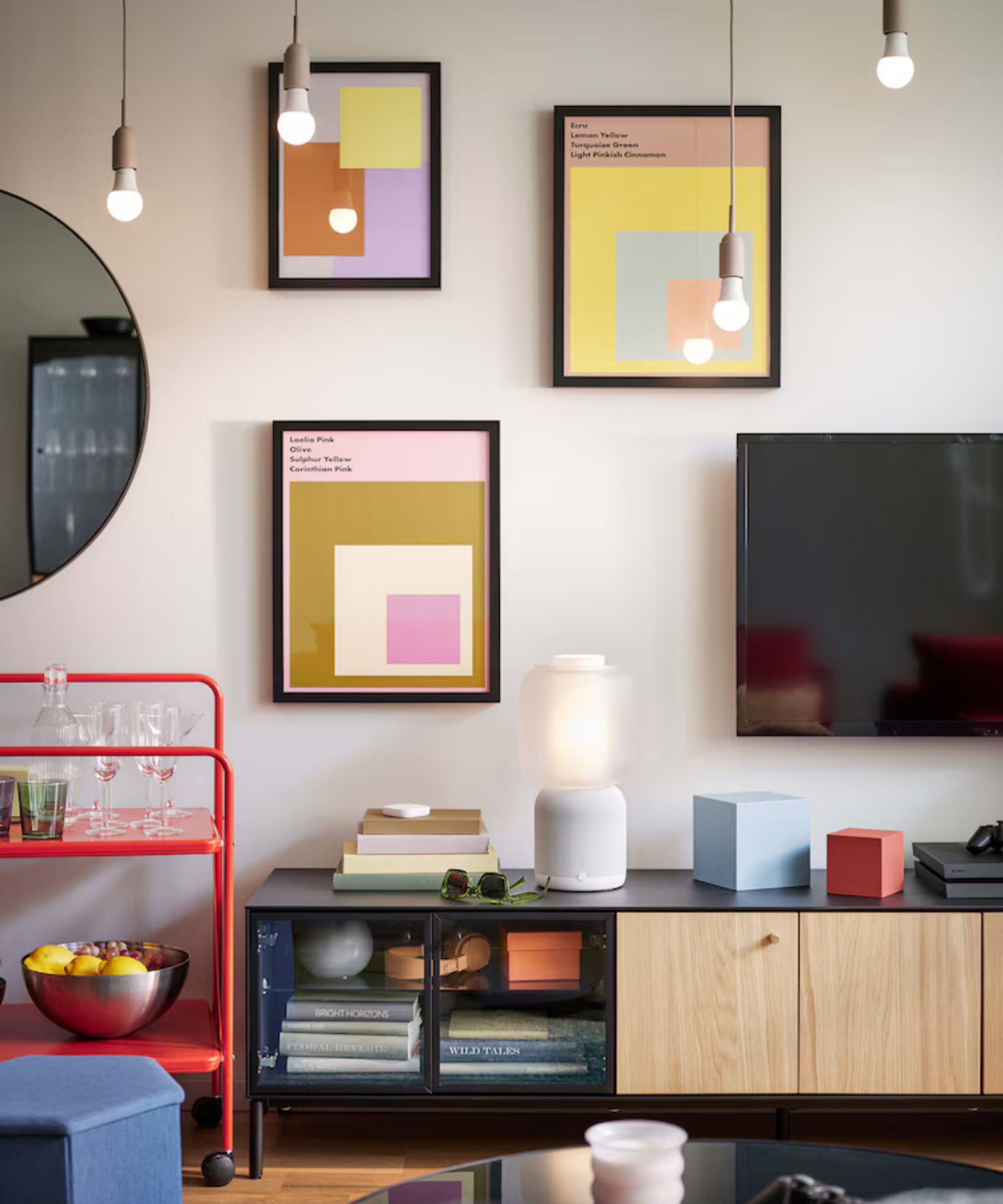 Salon ikea avec imprimés sur le mur et armoire télévisée basse en noir et bois avec chariot à barre orange néon