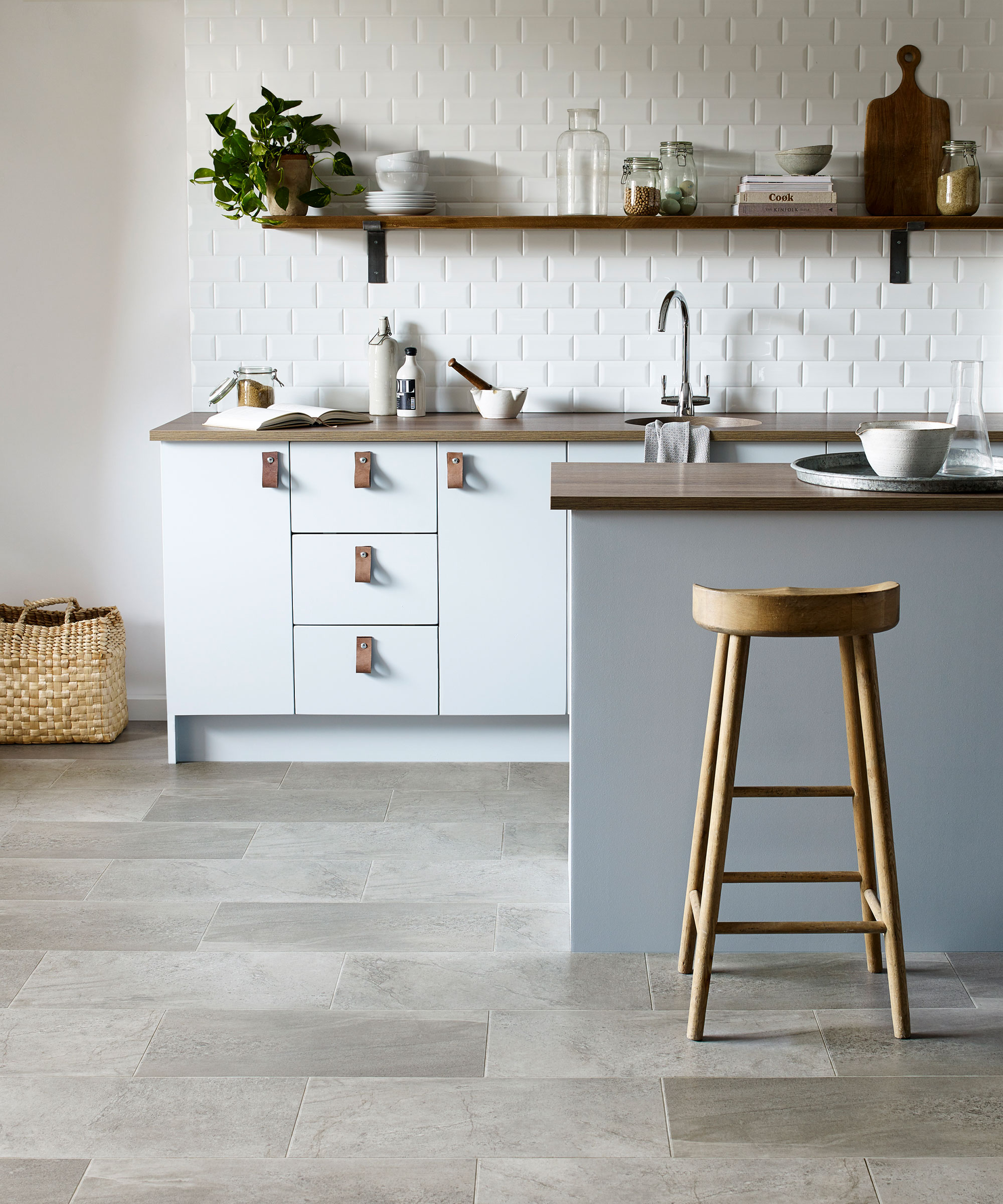 Espace de cuisine avec conception de carreaux de sol en vinyle en vinyle gris, îlot de cuisine peint gris foncé avec comptoir en bois foncé, placards de cuisine blanches avec poignées en cuir marron, étagères et comptoirs en bois foncé, tabourets de bar associés à l'île en bois
