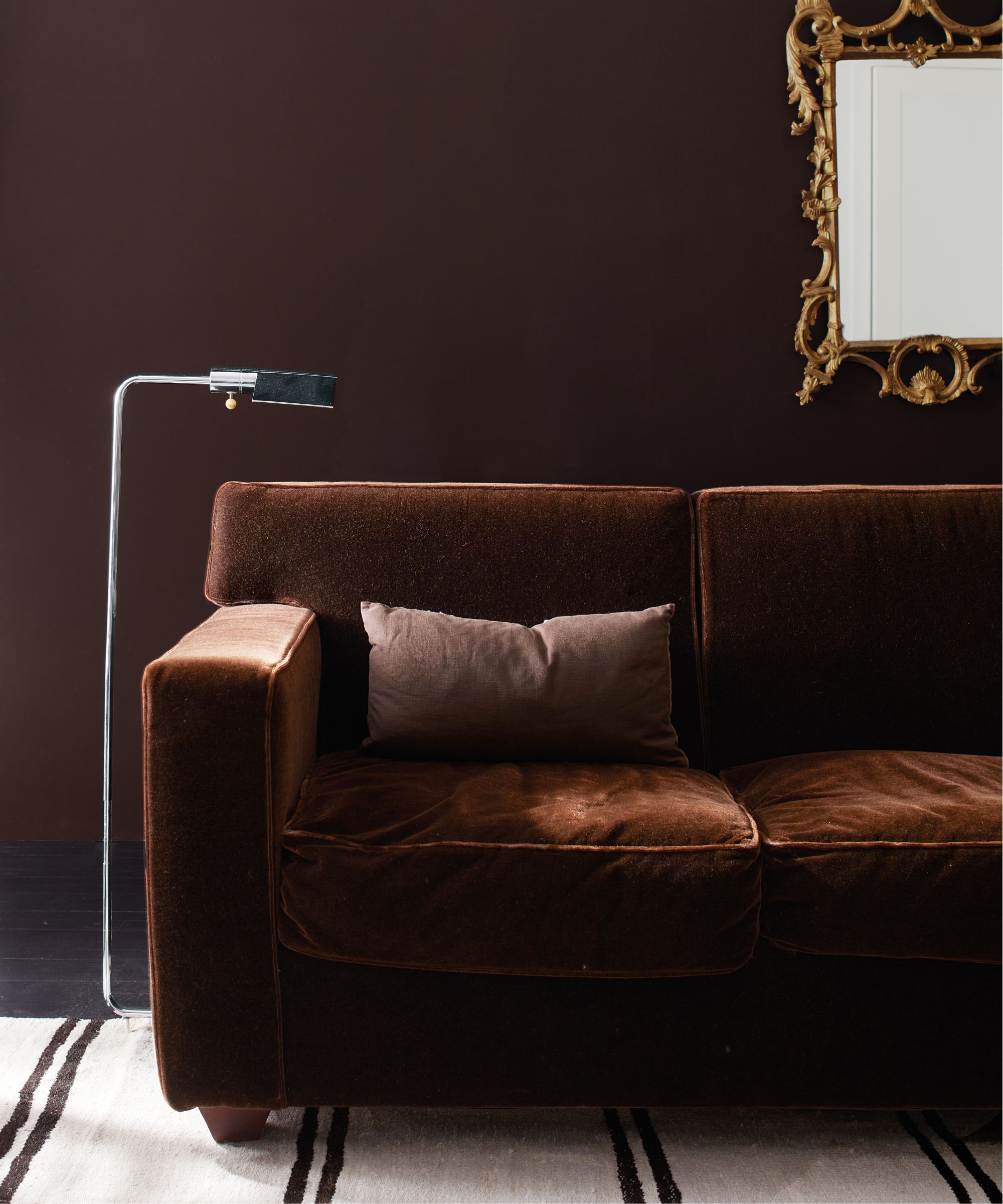 mur brun foncé dans le salon avec canapé brun en velours, miroir doré sur le mur