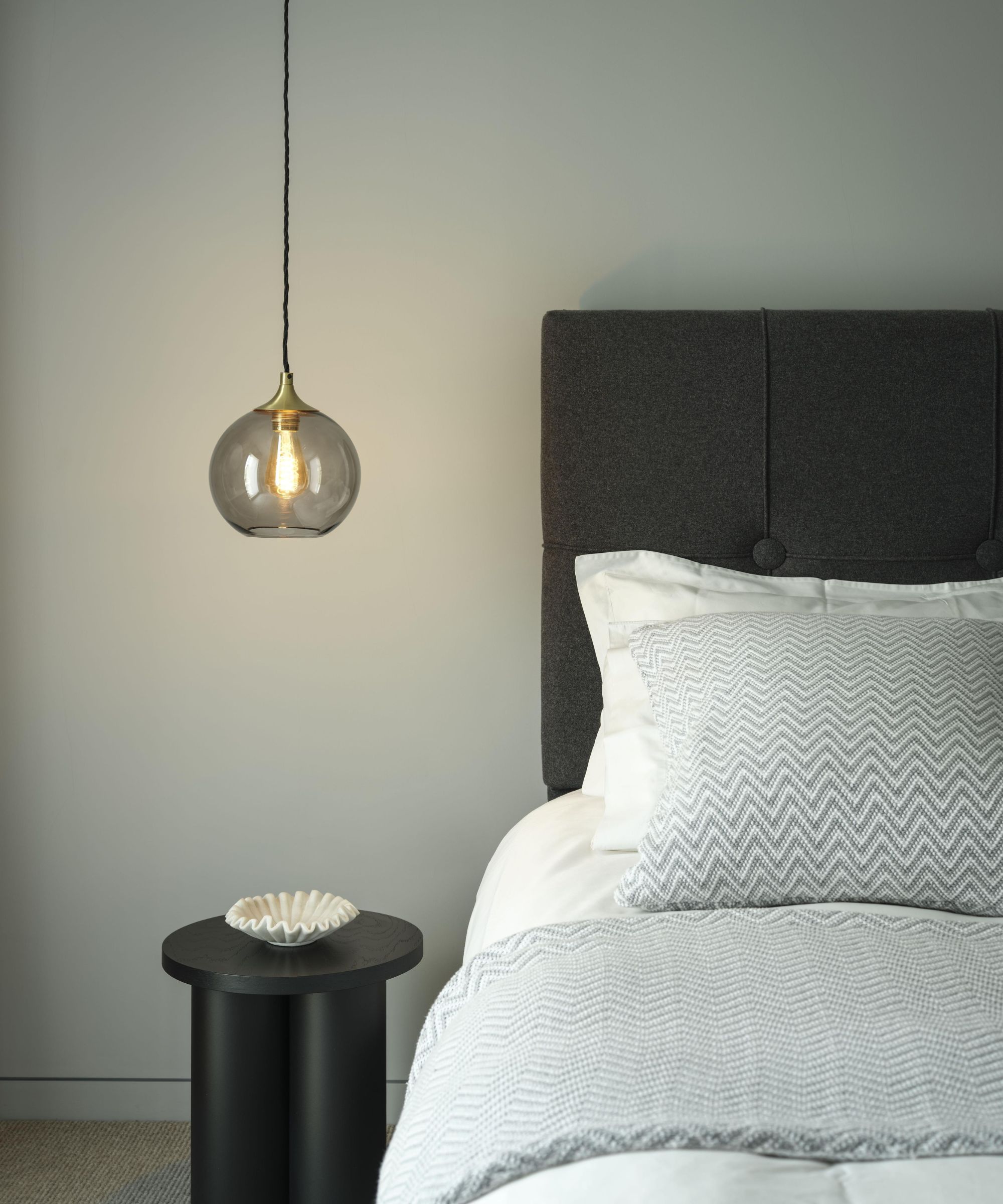 Chambre minimale avec lancer Chevron et oreiller assorti, table d'appoint ronde noire et lumière suspendue en verre suspendu