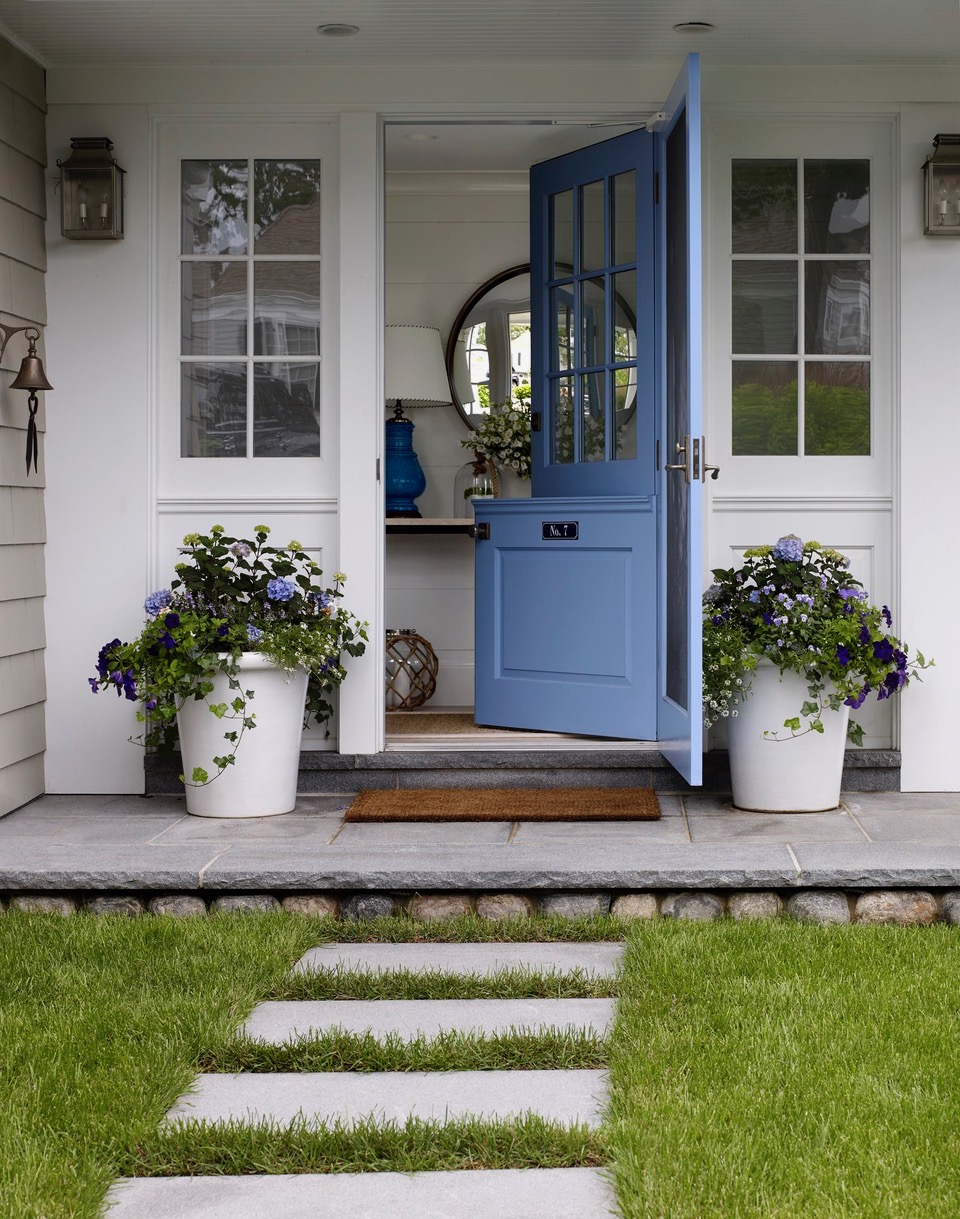 Porche avant avec des portes hollandaises bleues, des fleurs en pot, de l'herbe et du patio
