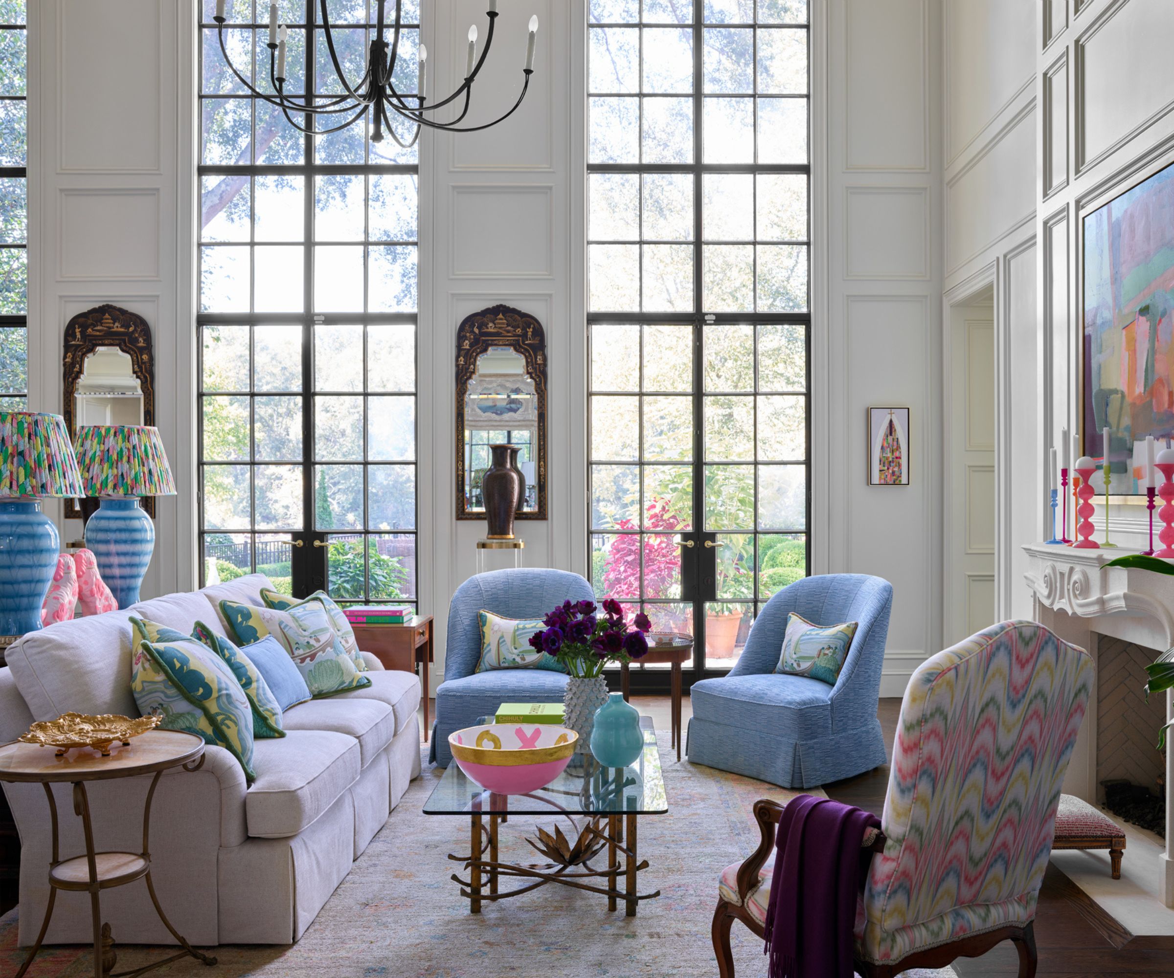 Grand salon avec de hautes fenêtres, murs blancs en lambris, pops pf bleu et rose décor coloré