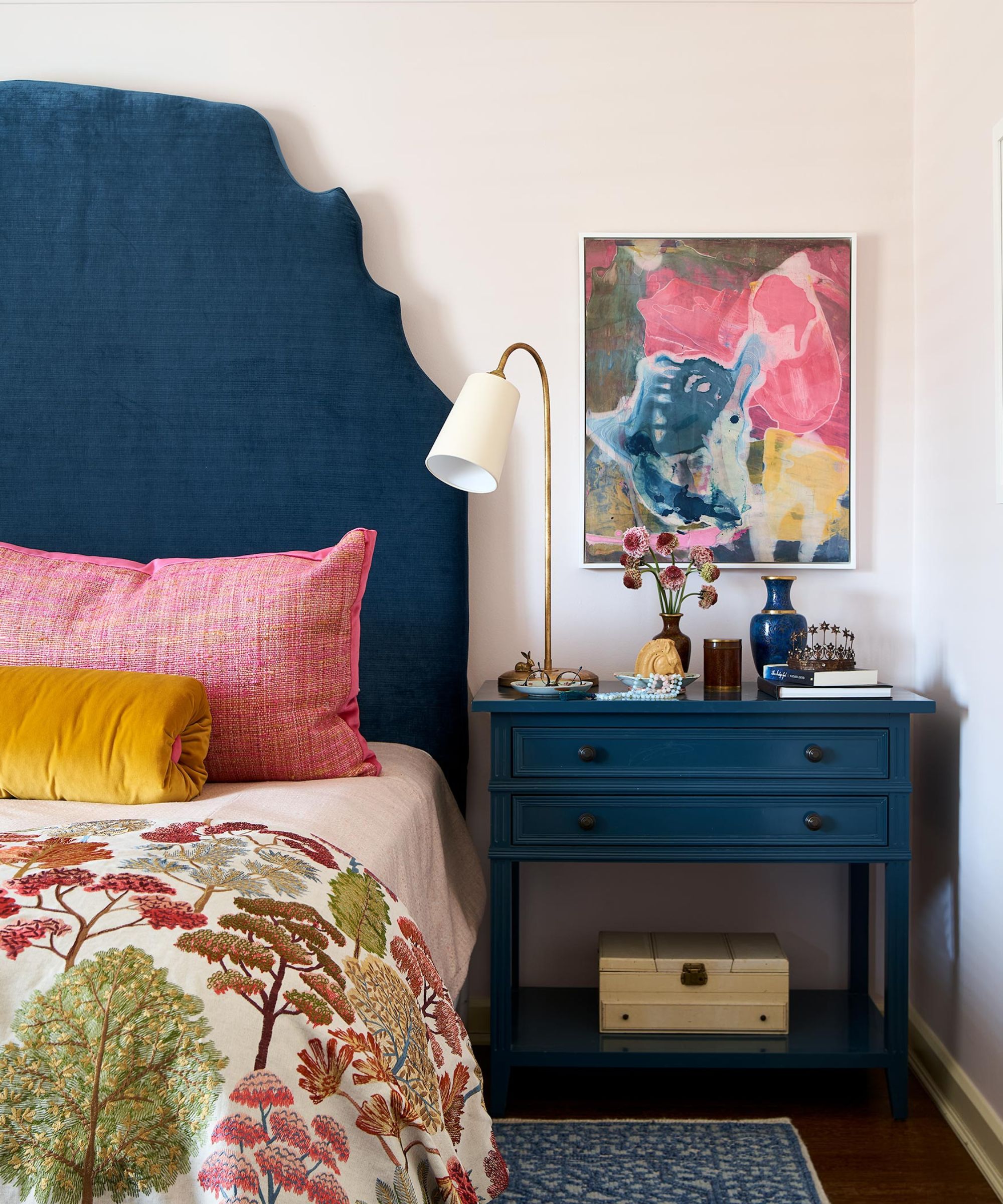 chambre à coucher avec tête de lit marine, table de chevet bleu marine, œuvres d'art rose et oreillers