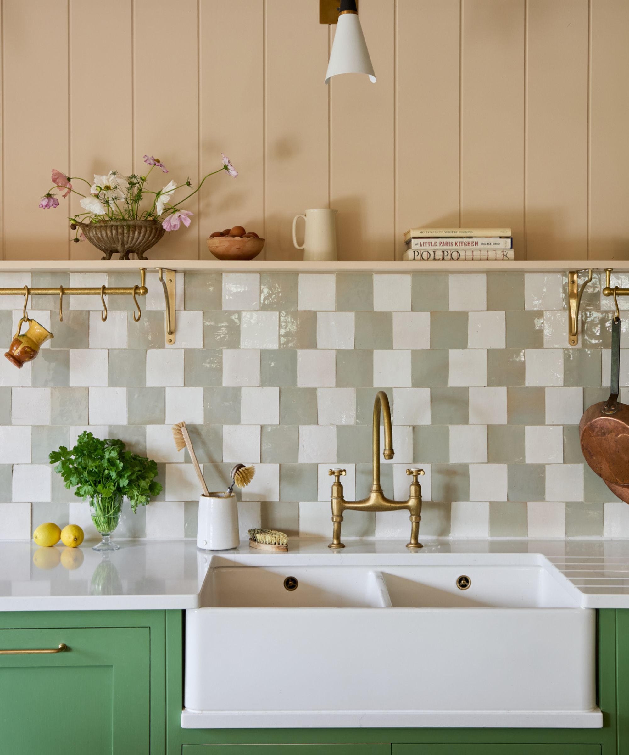 Cuisine verte avec dosseret en damier zellige vert et blanc pâle, évier majordome et un mur et une étagère lambrissés de pêche rose pâle au-dessus