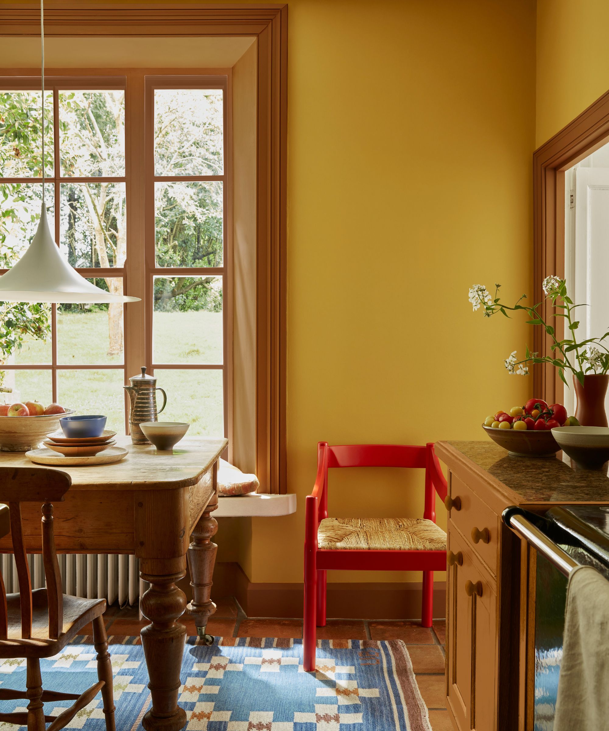 Cuisine jaune avec tapis tissé bleu, chaise peinte en rouge, table à manger en bois et chaises et feu de pendentif bas