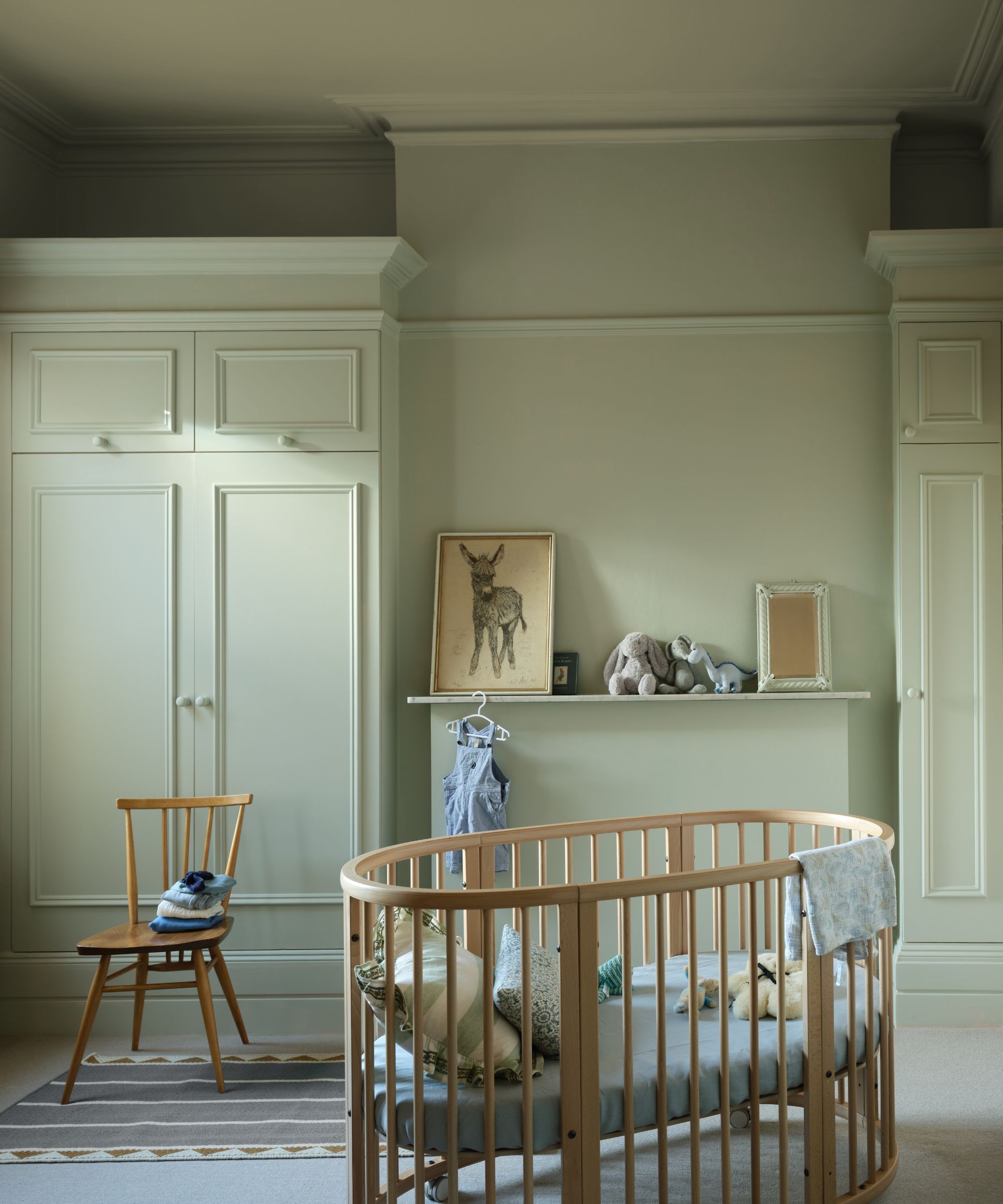 Une crèche d'enfant avec un lit de lit, une chaise et des armoires construites. Les murs sont peints dans un vert pastel pâle très délicat.