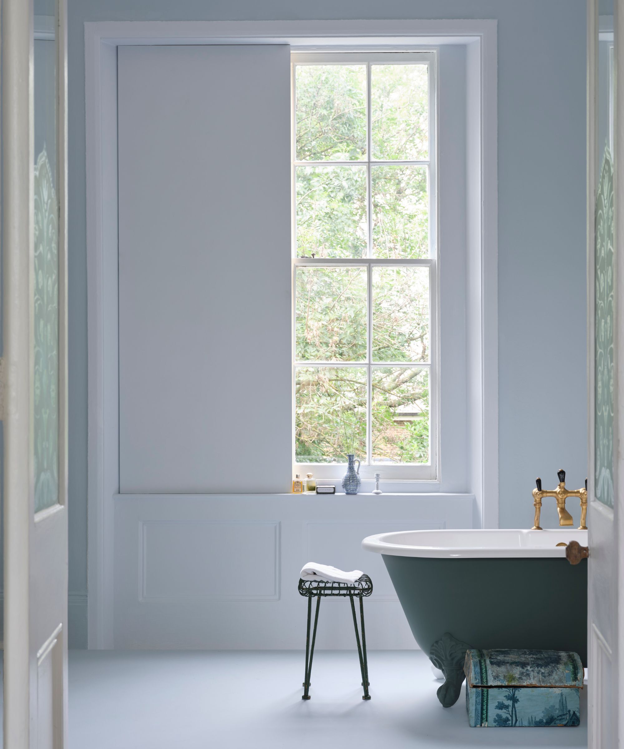 Une grande salle de bain avec une baignoire à roulis et des fenêtres à ceinture. Les murs de la salle de bain sont peints dans une peinture bleu pastel très pâle.