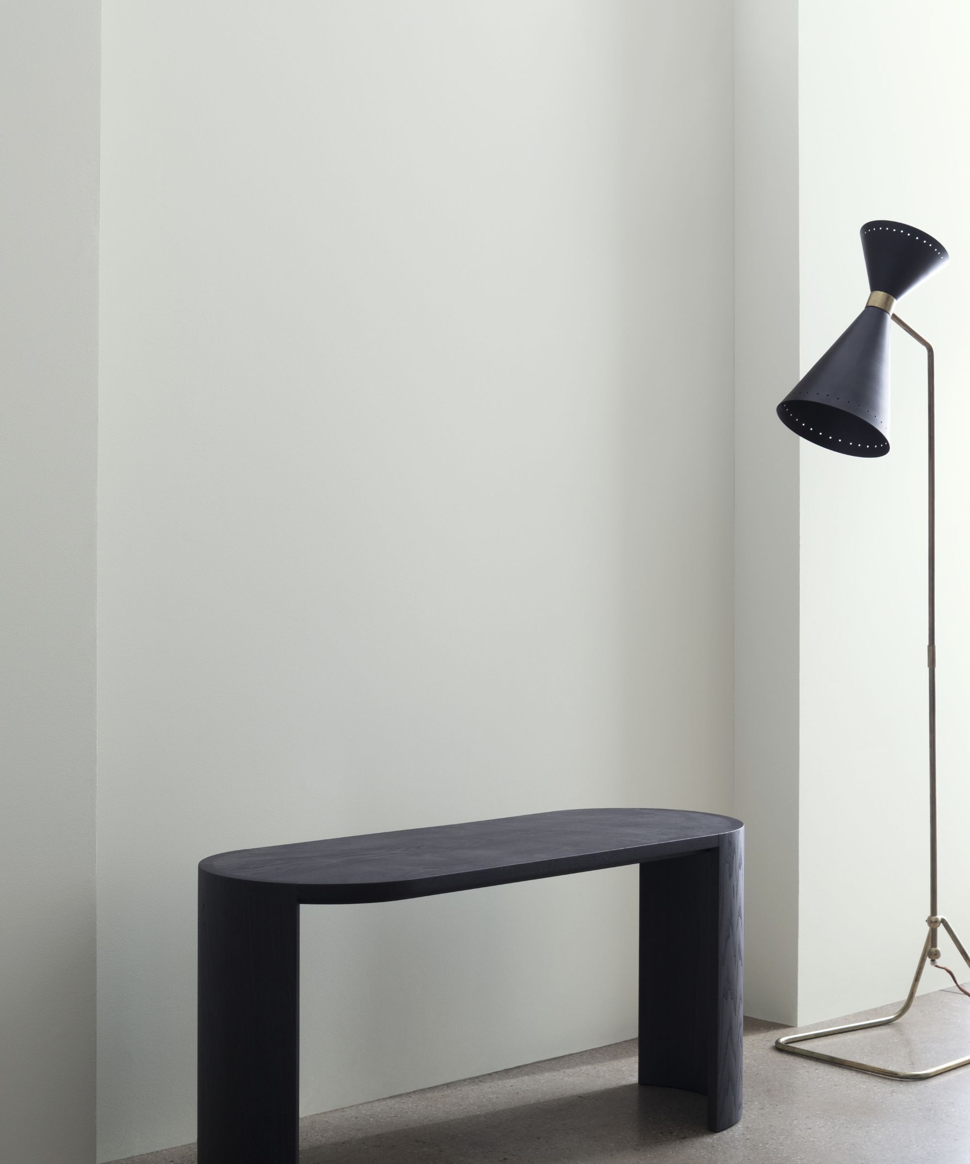 Une pièce avec une lampadaire noire et un banc noir, le mur peint dans un gris crémeux.