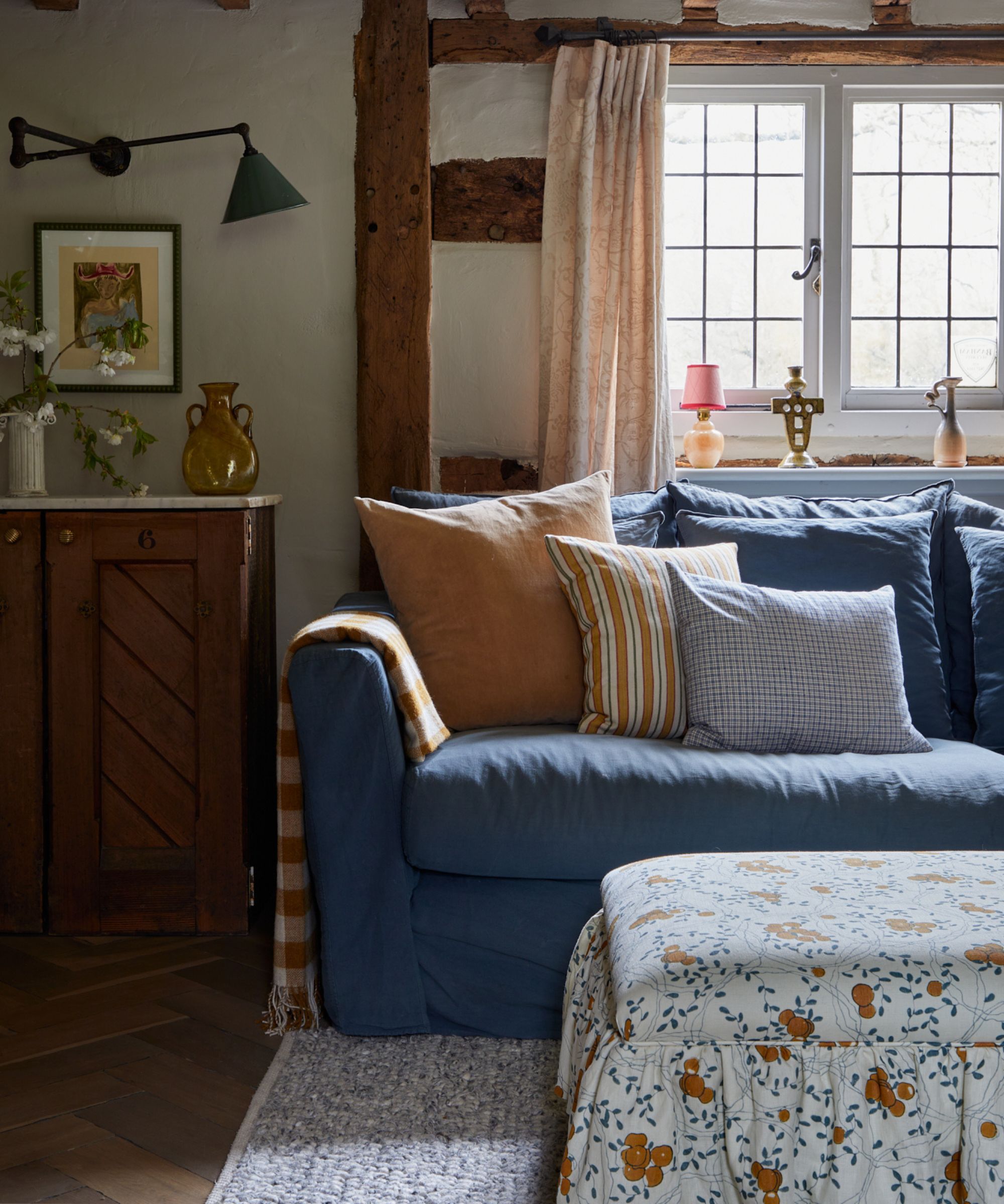 salon cottage avec plafonds à poutres basse et canapé bleu marine avec coussins rayés et ottoman à jupe floral bleu blanc et orange
