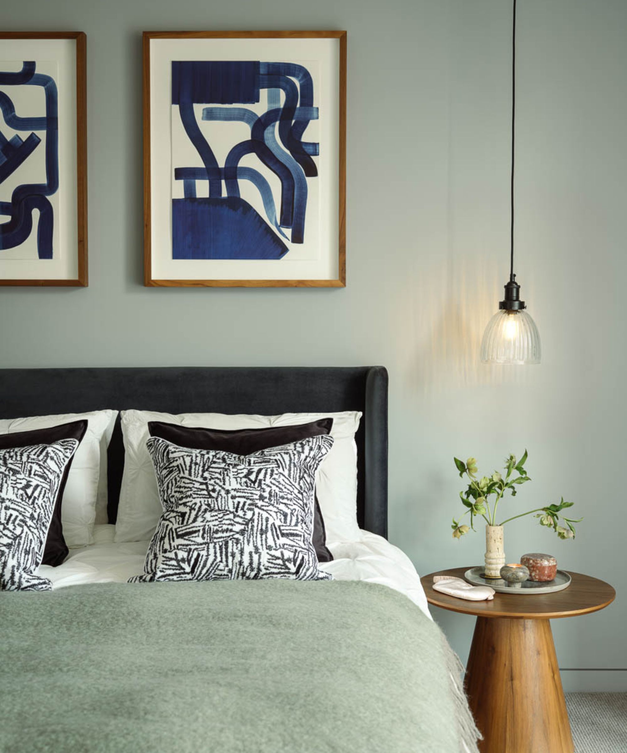 Chambre moderne avec art abstrait sur mur, lit avec lancer duveteux et table de chevet ronde en bois avec feuillage et pendance suspendue