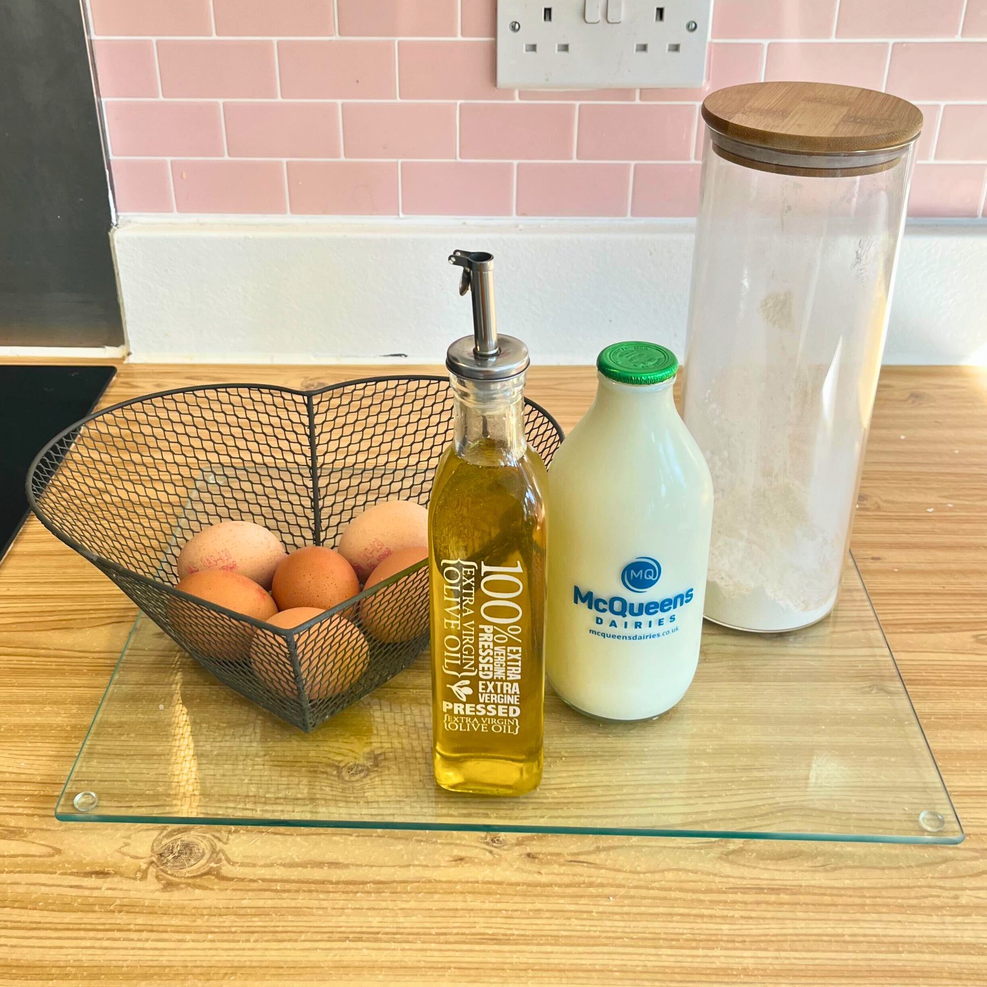 Comptoir de cuisine en bois avec un panier d'œufs en métal de coeur et des récipients en verre avec du lait, de l'huile et de la farine
