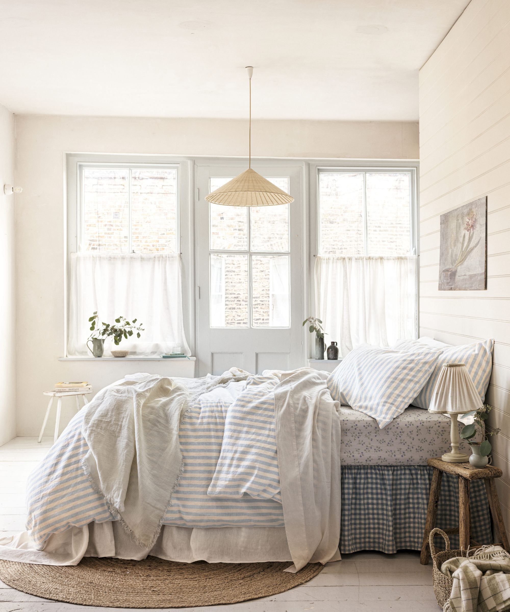 Chambre esthétique des pêcheurs avec un lit en couches avec une jupe de lit de vichy, une literie rayée, des draps floraux et des murs de la chambre à chapeaux