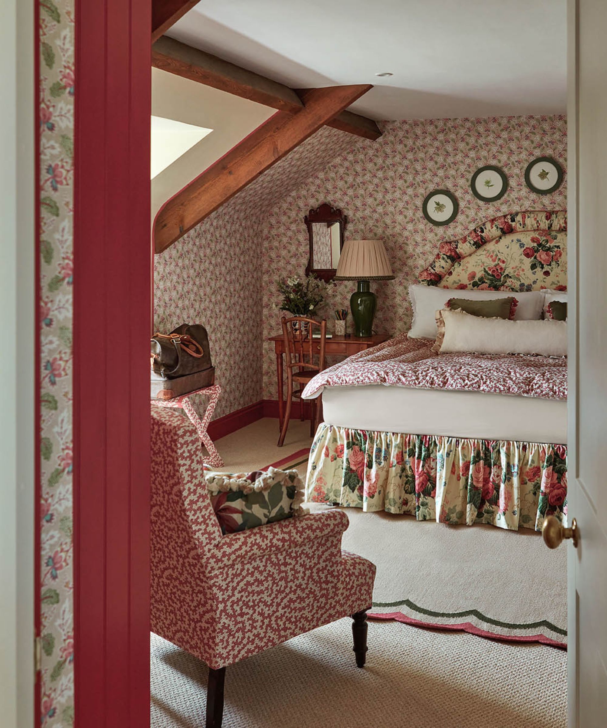 Chambre de papier peint grenier avec un plafond à poutres basse et une tête de lit à fleurs avec une jupe de lit assortie assise sur un tapis festonné
