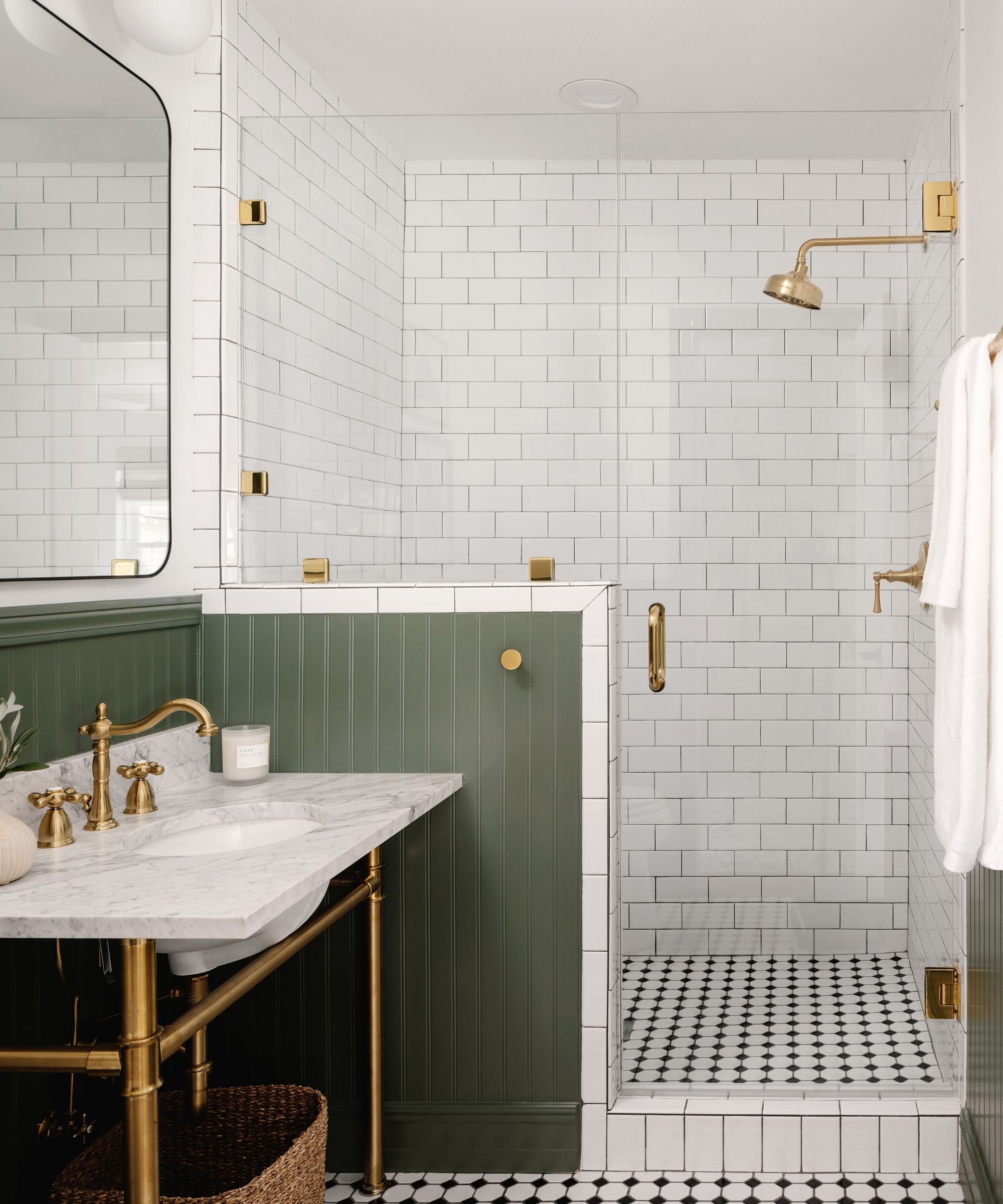 Salle de bain carrelée en métro avec sol en mosaïque, boiseries en bois vert, évier en marbre avec robinets en or et grand miroir
