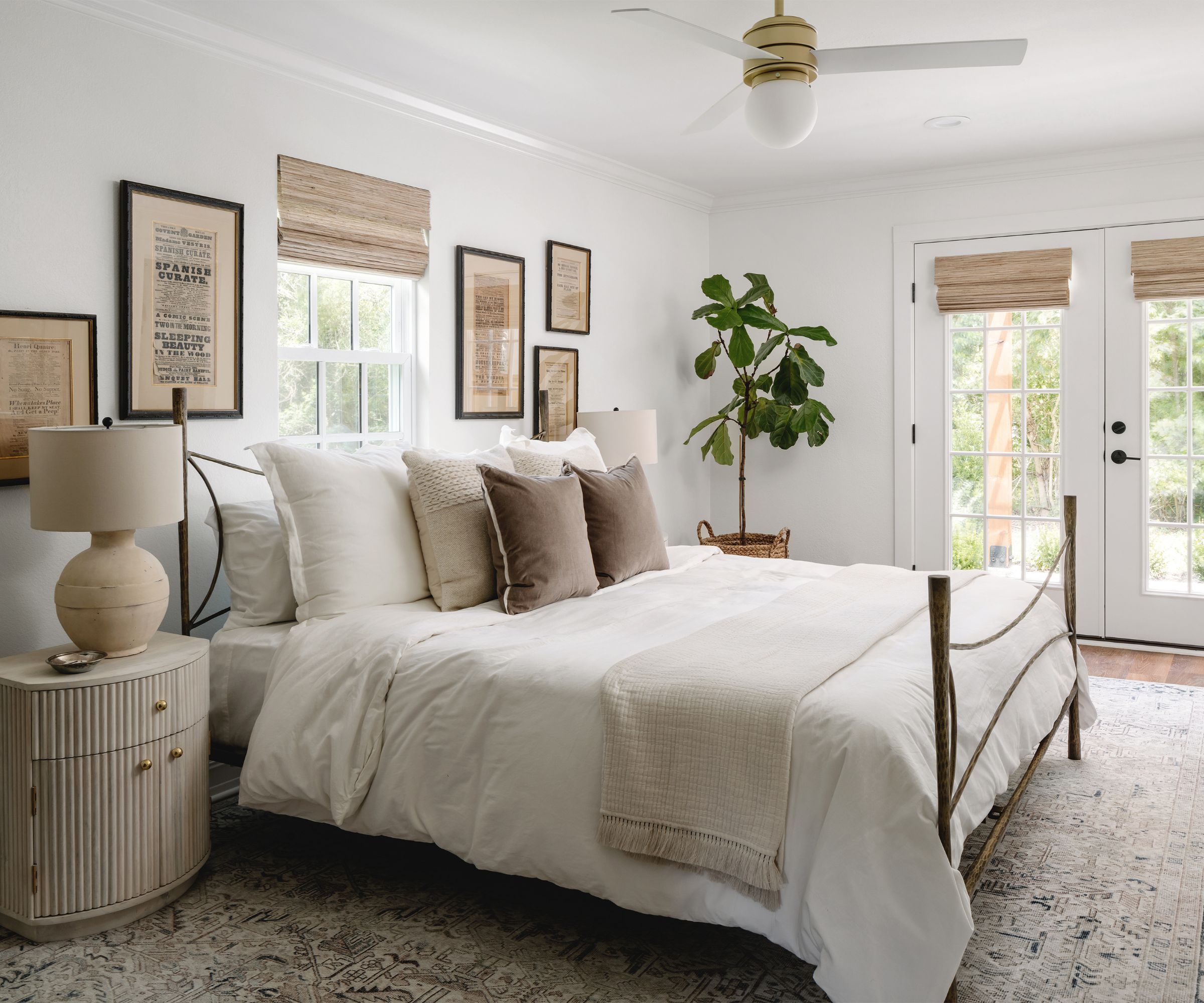 Chambre neutre avec grand tapis, cadre de lit en fer avec linge neutre en lin, art mural vintage et grande plante dans le coin