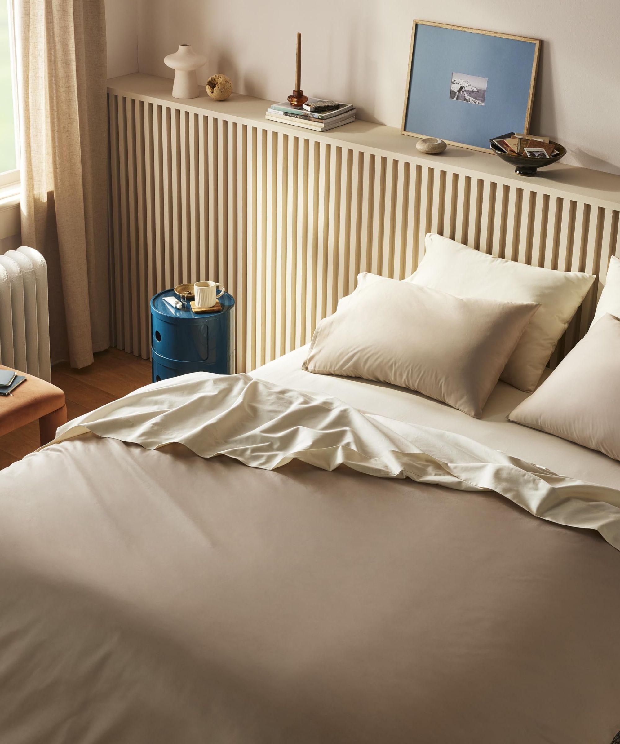 Vue à l'œil de l'oiseau de la literie beige et brune sur un lit contre les murs crème avec de l'art mural bleu.