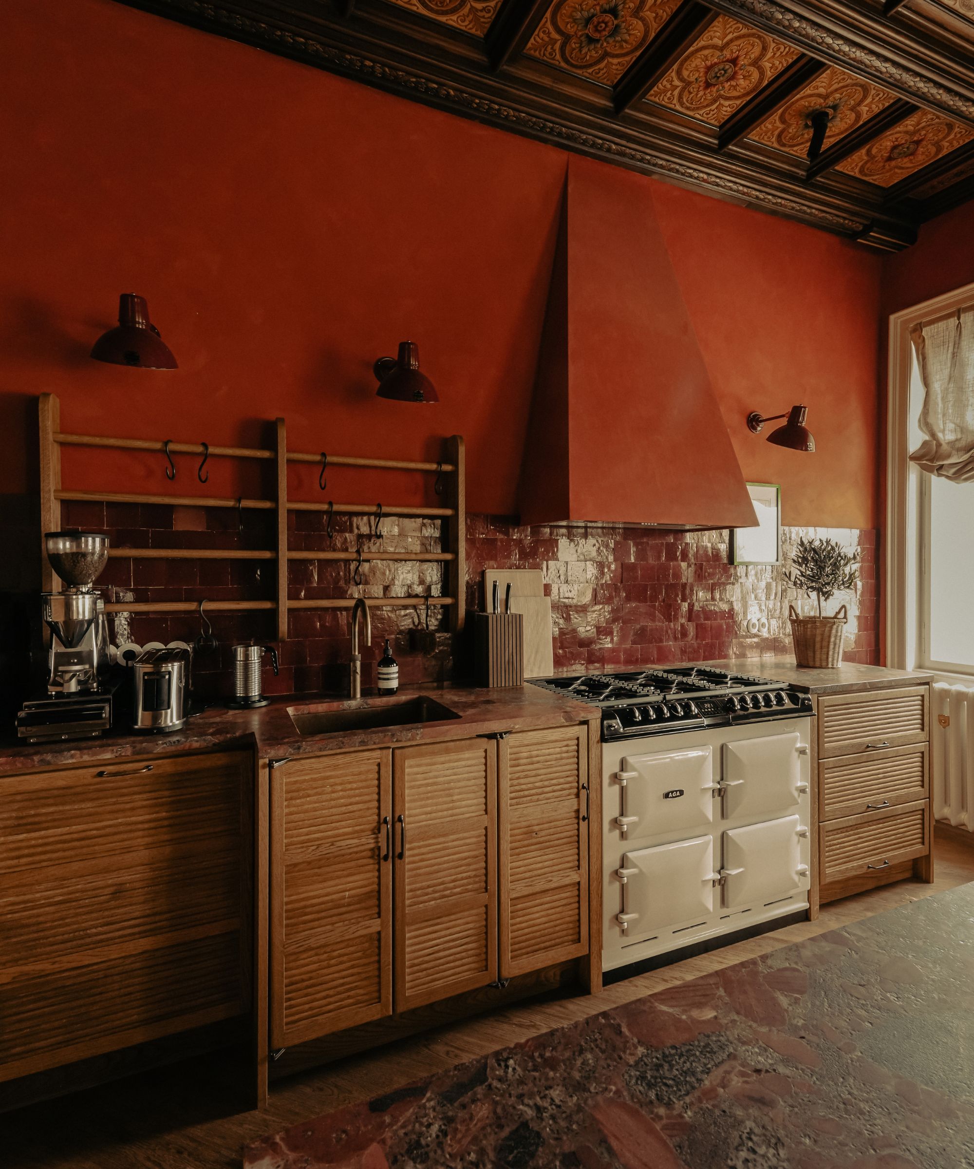 Une cuisine avec des murs paprika, des carreaux de dosseret bordeaux, des armoires en bois et un Aga blanc