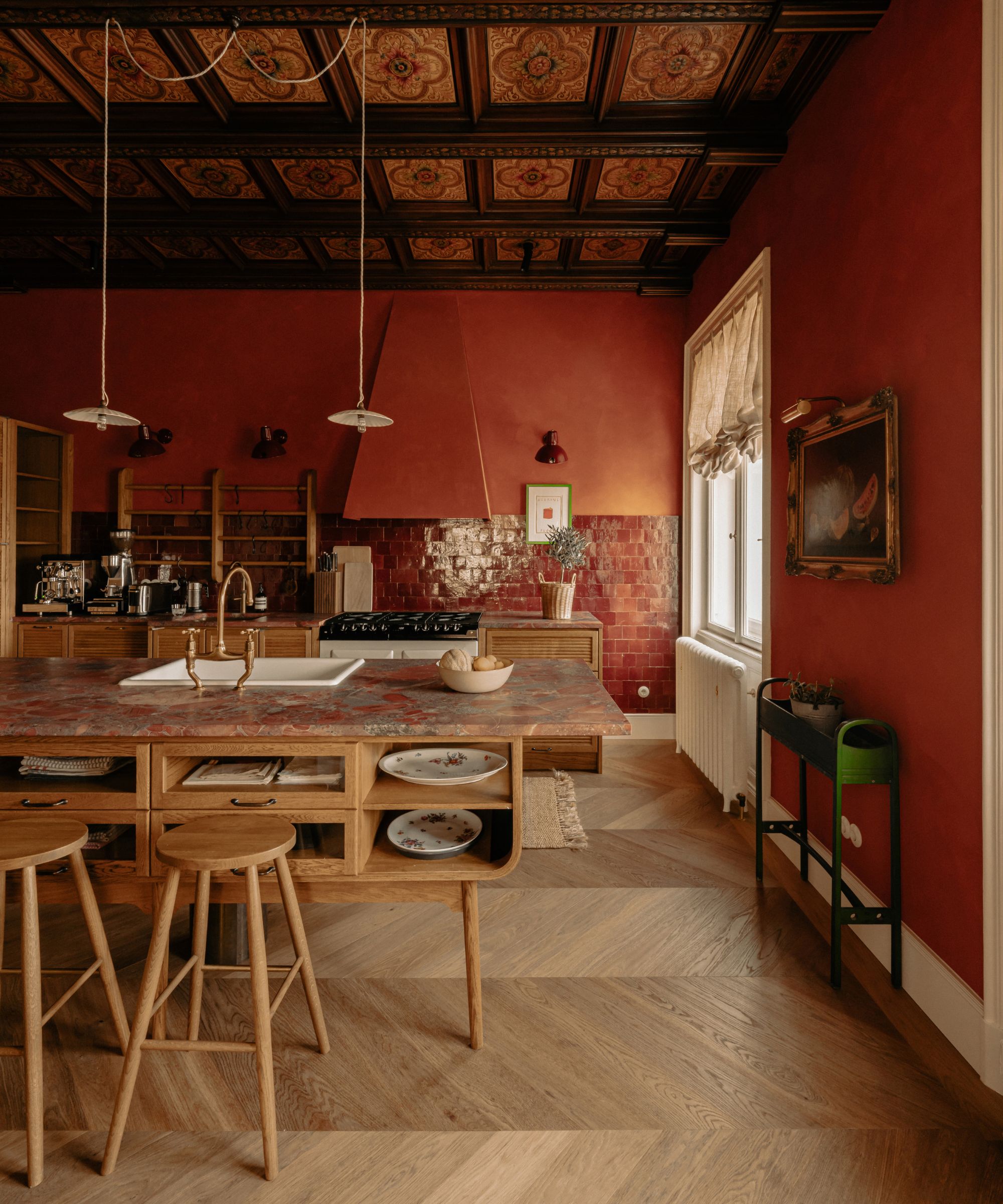 Une cuisine avec des armoires en bois, un îlot de cuisine indépendant en bois, un parquet en bois, des murs rouges paprika et un cieling lambrissé d'origine