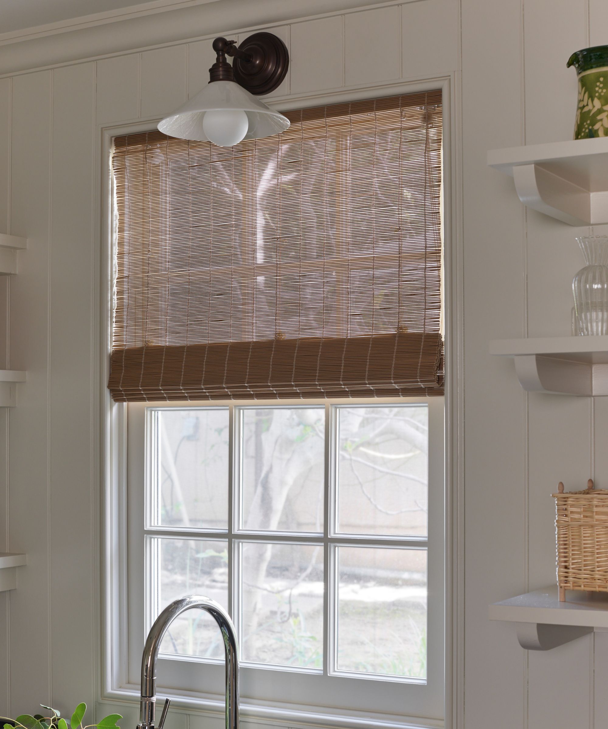 Cuisine petite fenêtre avec des murs en lambris blancs et un aveugle tissé de matchstick de l'Everhem x cette collaboration en chêne avec une petite apponce murale de style vintage suspendu au-dessus de la fenêtre
