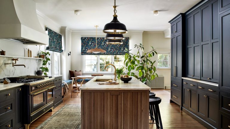Cette cuisine autrefois datée est désormais un espace intemporel avec les détails les plus confortables – et c’est la palette de couleurs classique qui en fait un espace chic et accueillant A kitchen with dark blue cabinets, white walls, a wooden island, and a dining nook with banquette seating