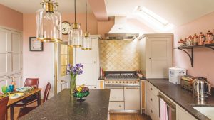 5 pièces vintage que chaque cuisine devrait avoir, selon les concepteurs Kitsch pink kitchen with yellow shel-shaped backsplash tiles behind cream and gold range cooker. It's a kitchen diner with breakfast bar and gold accented pendant lights
