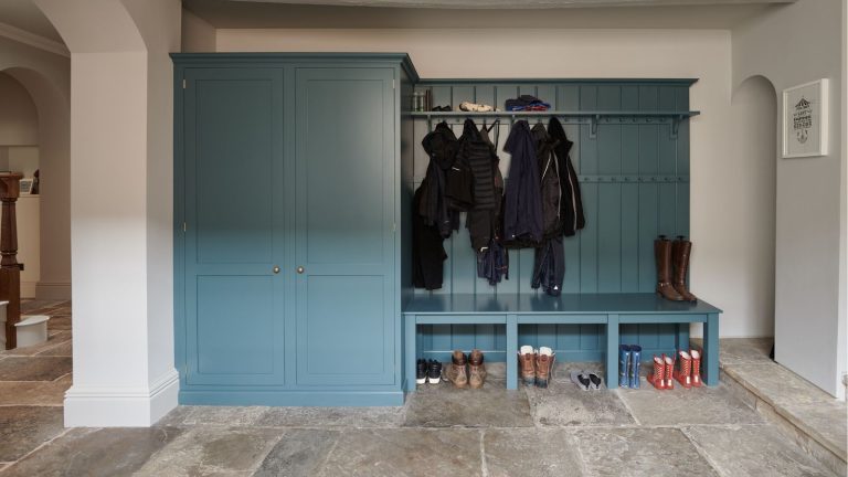 Mud room with blue cabinets and stone floors, coats hanging up on built in rail hooks.