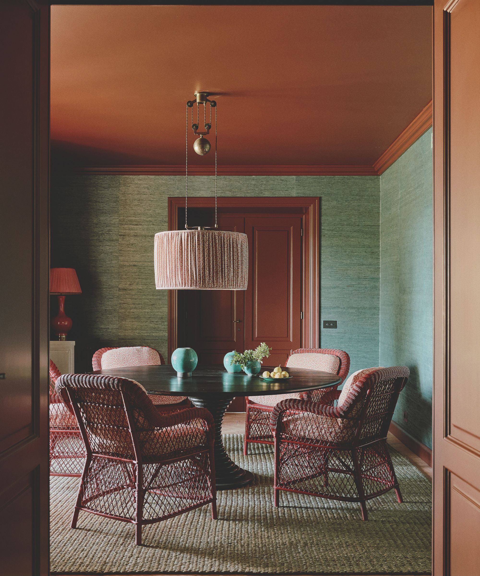 Salle à manger avec chaises en rotin, table circulaire et plafond orange avec des murs verts