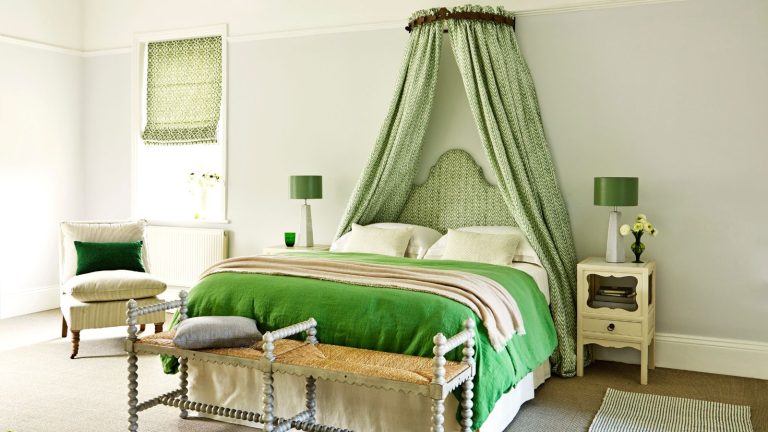 Bedroom, green theme, corona with herrigbone fabric and matching headboard in white wall with armchair, bedside tables, green lamps, rugs and small table at the foot of the bed.
