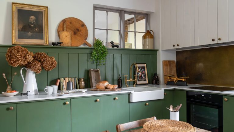 A green traditional country kitchen, with a farmhouse sink and a copper splashback behind the stove.