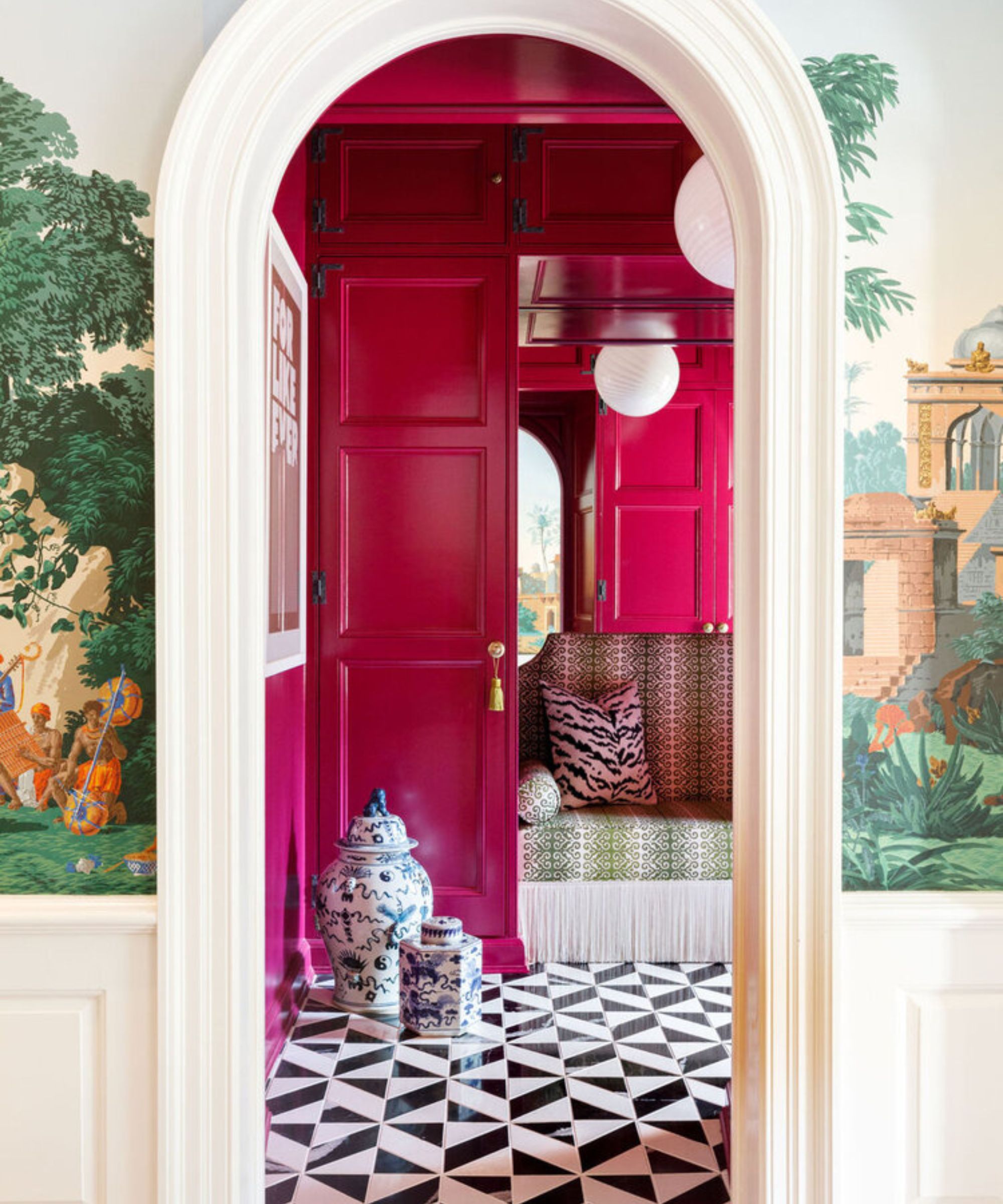 Vue à travers une arche dans une salle de manteau à murs brillant rose avec un sol noir et blanc et un mur en miroir