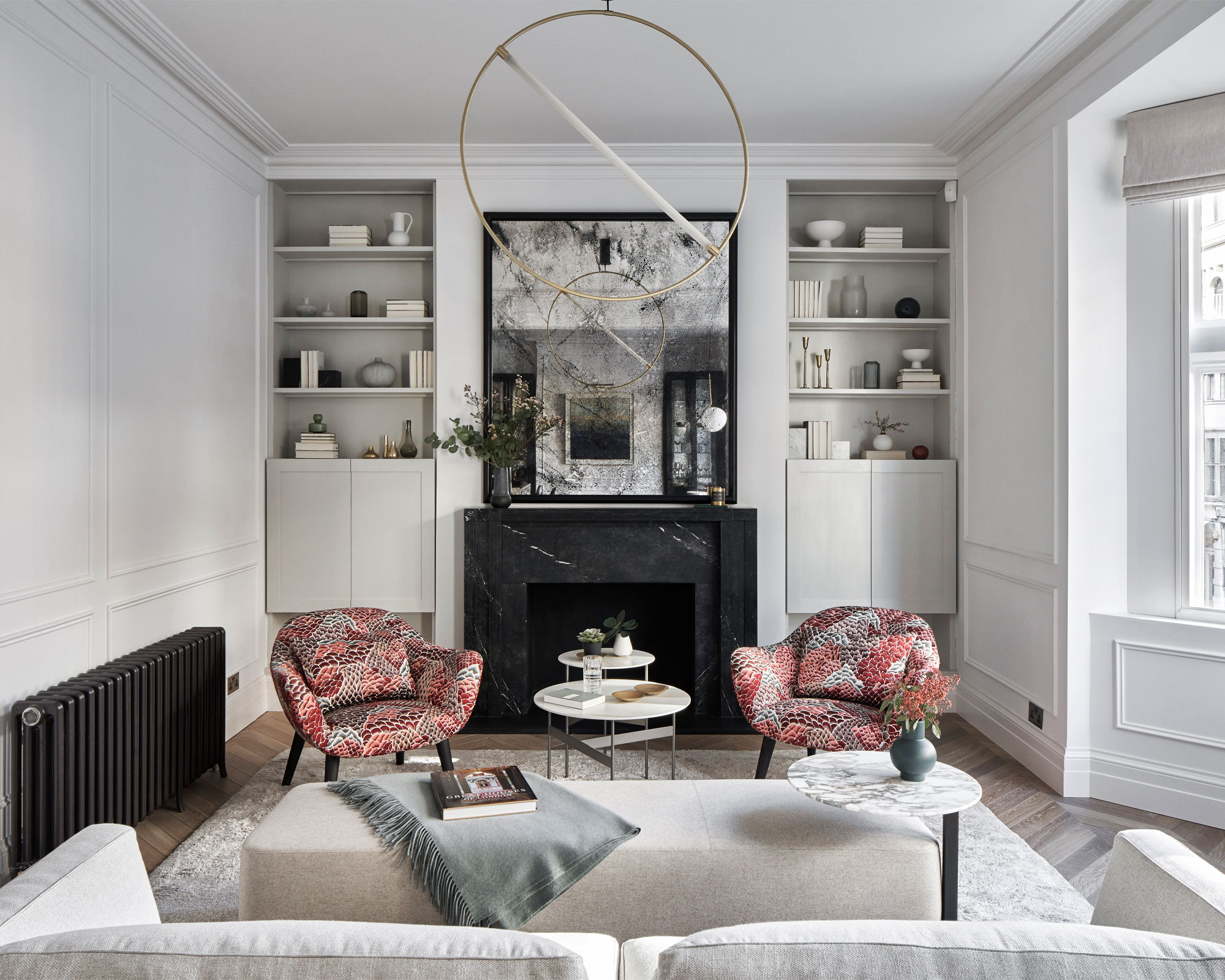 Salon avec des murs gris pâle, une baie vitrée, intégrée en stockage de chaque côté de la poitrine et de la cheminée de la cheminée. Tapis gris et canapé et fauteuils à motifs orange.