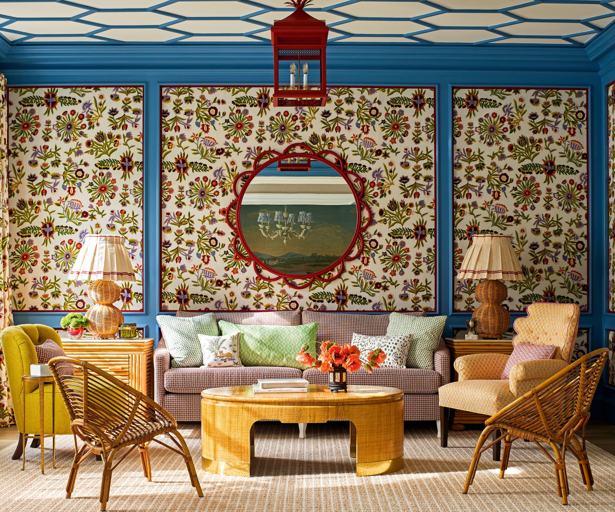 salon avec un papier peint à motifs et des panneaux bleu vif et des fauteuils jaunes et un canapé et une table de cofffee et un miroir circulaire rouge